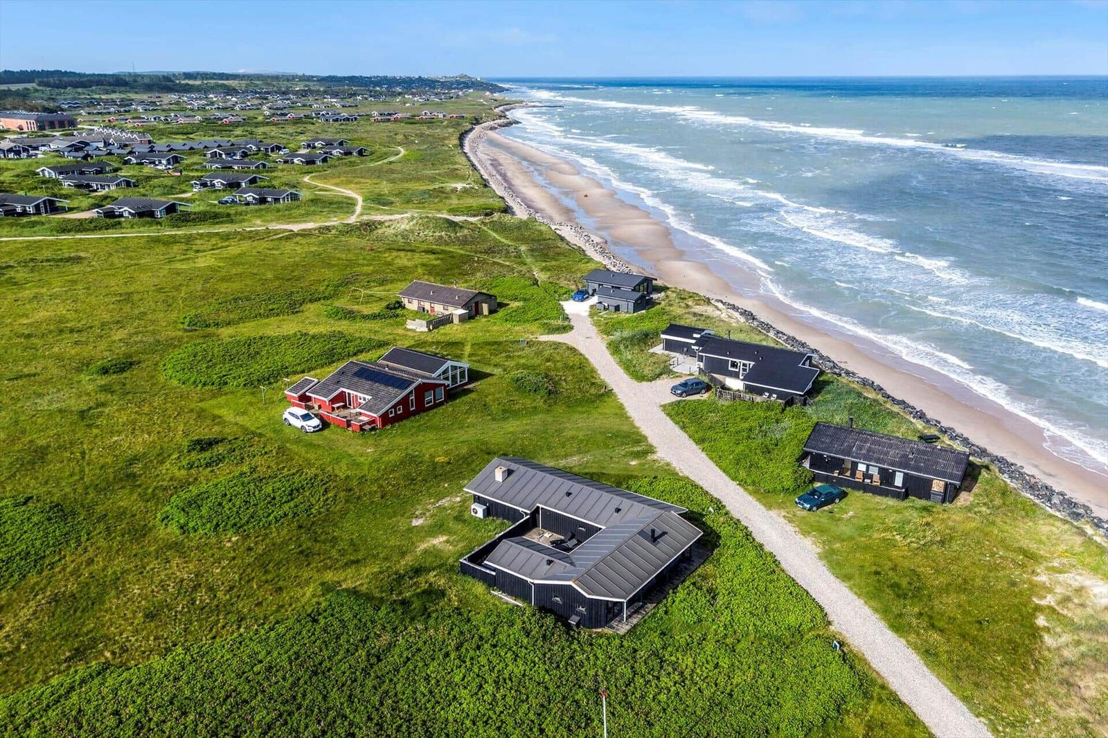 Aerielansicht von Strandhäusern auf grünem Gelände neben dem Meer.