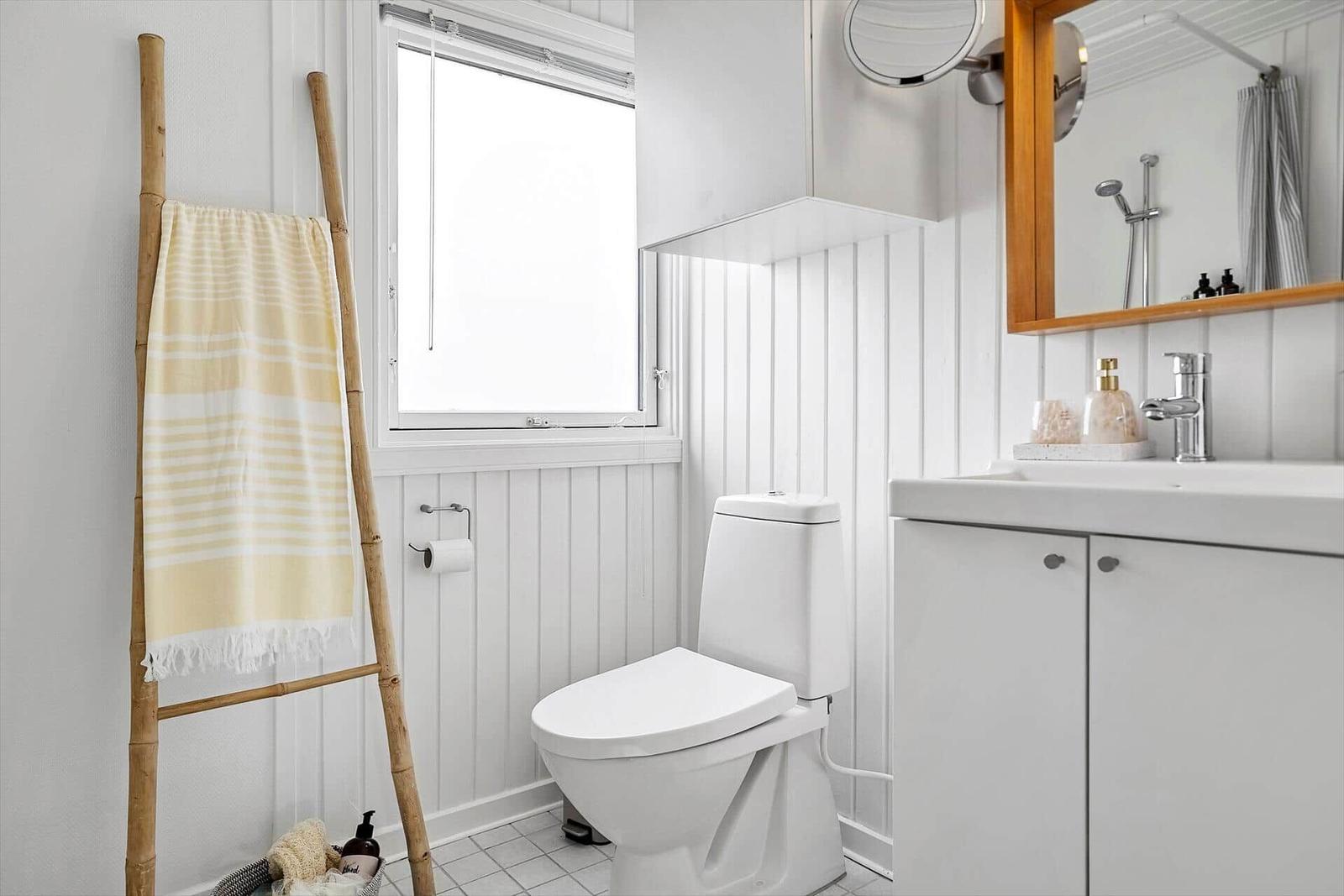 Badezimmer mit Toilette, Waschbecken und Fenster. Gelber Handtuchhalter und Spiegel.