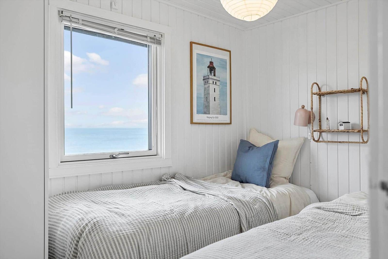 Schlafzimmer mit Blick aufs Meer, weiße Wände, Bett mit Kissen und Wandbild.
