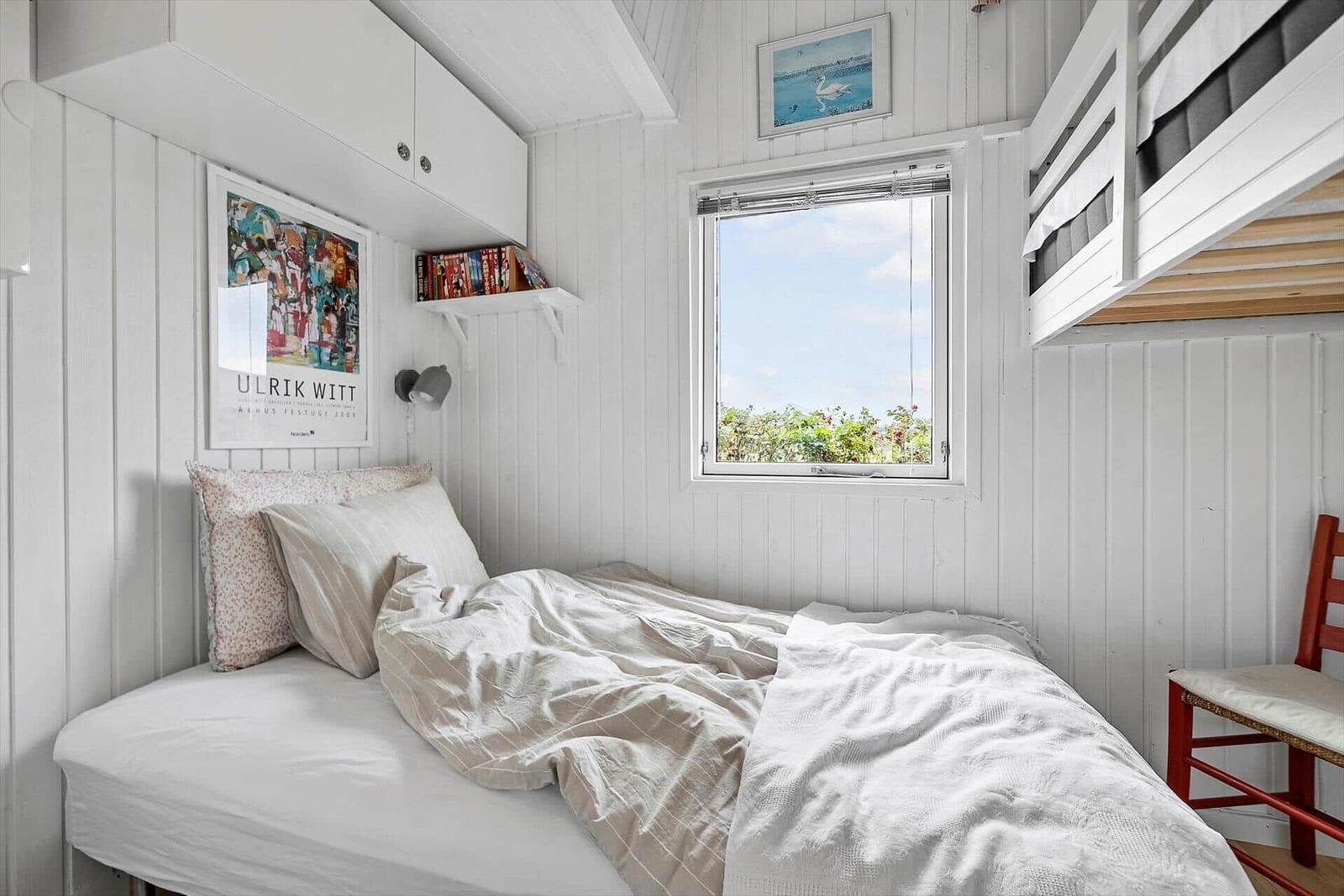 Ein Schlafzimmer mit Doppelbett, Fenster und Oberbett. Wandverkleidung und Poster sichtbar.