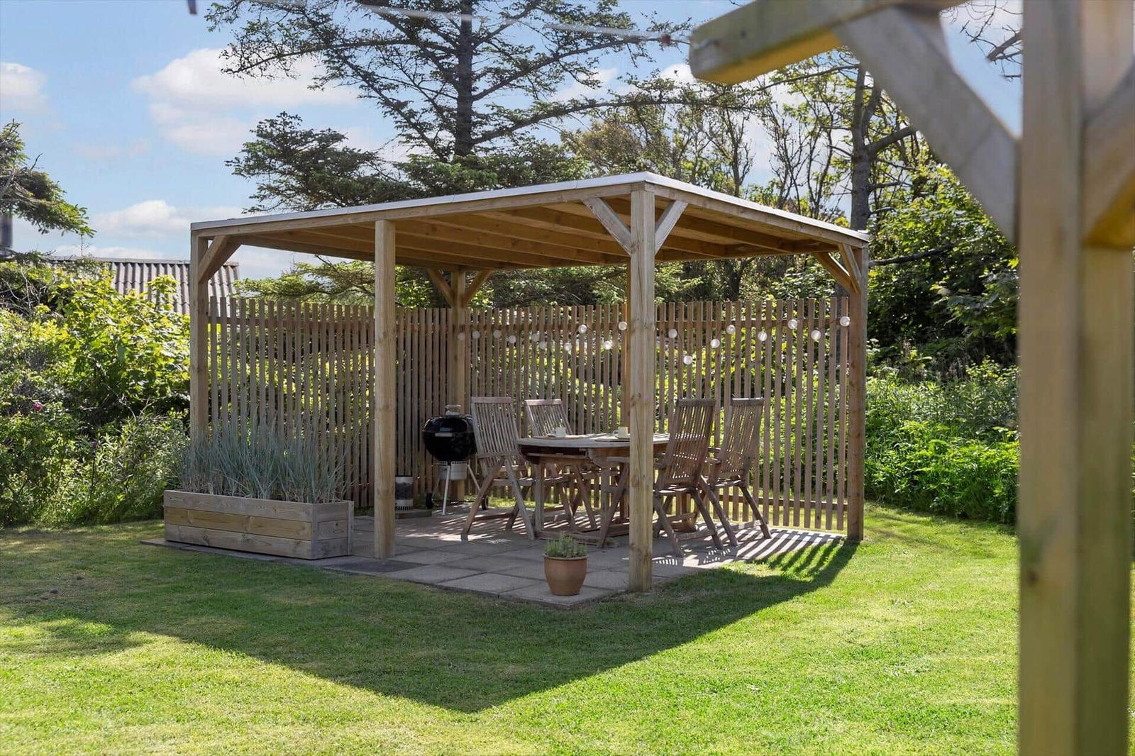 Holzüberdachung mit Tisch, Stühlen und Grill im Garten