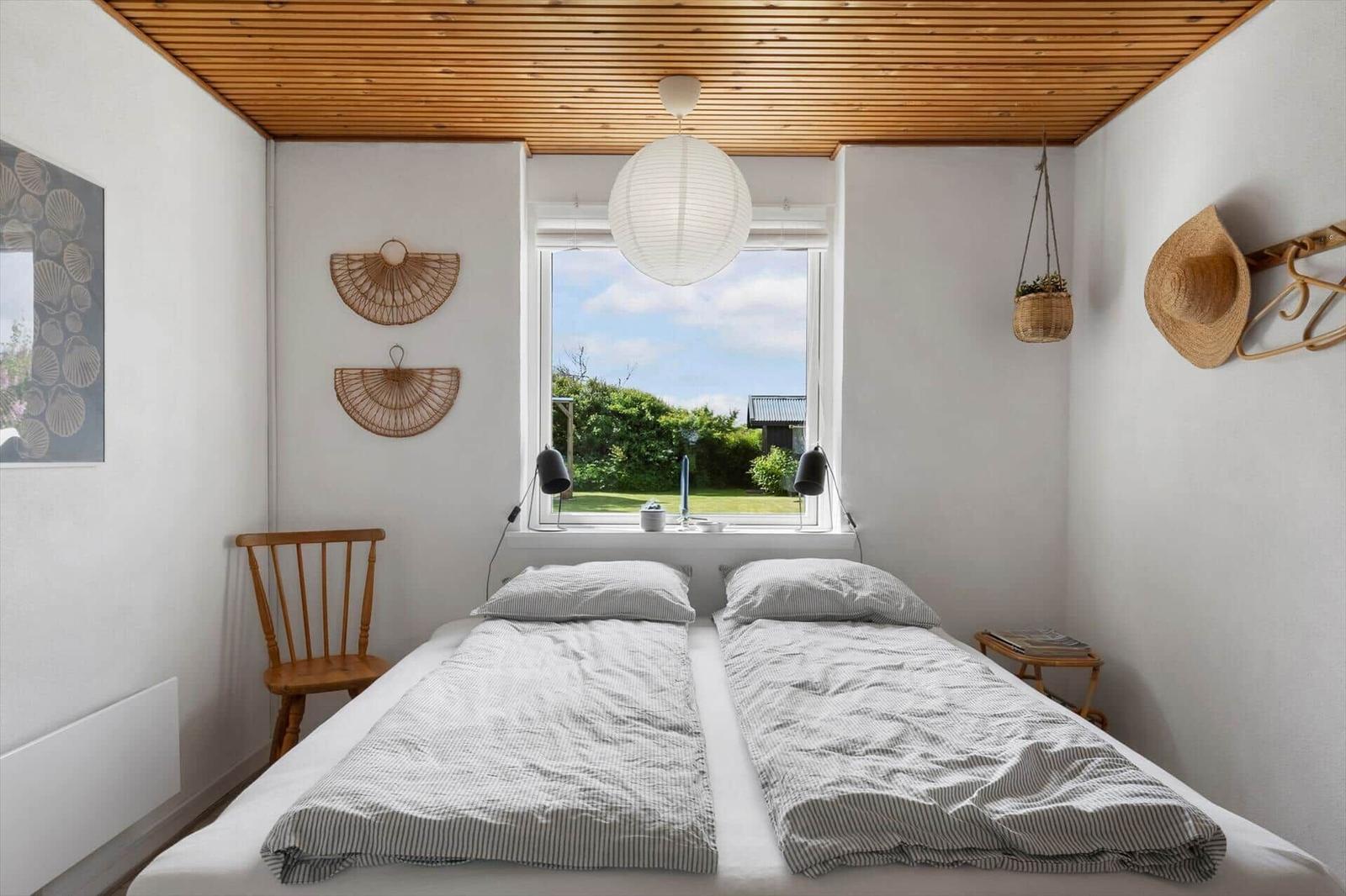 Zimmer mit Doppelbett, Fensterblick auf Garten, Holzdecke und Wanddekoration.