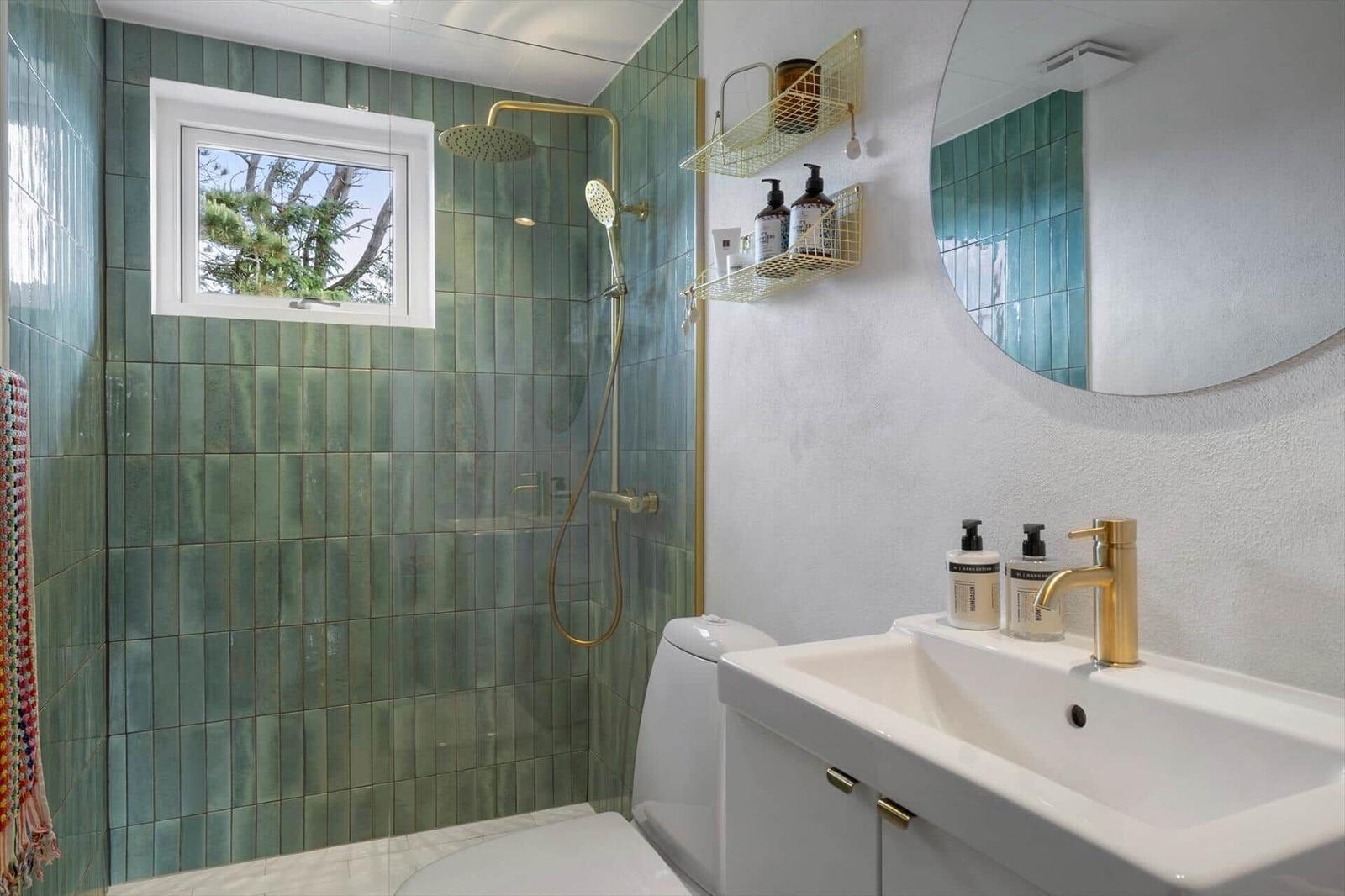 Badezimmer mit grünen Fliesen, Dusche, Waschbecken und Spiegel.
