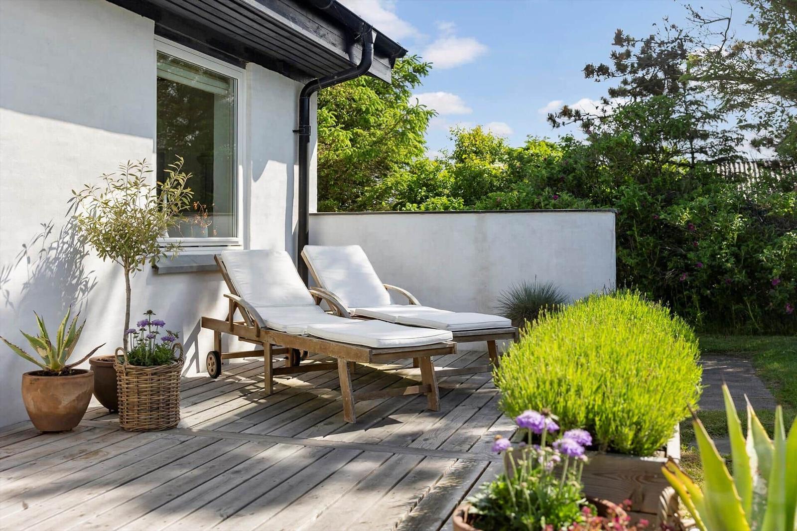 Terrasse mit zwei Liegestühlen, Pflanzen und Blick auf grüne Bäume.