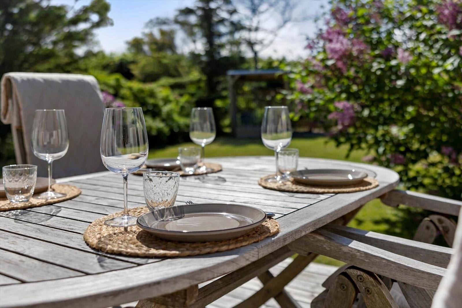 Rundtisch mit Tellern und Gläsern im Garten mit Blumen und Grün.