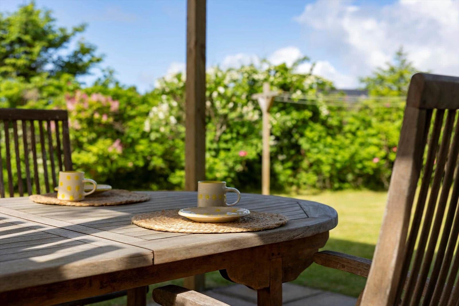 Holztisch mit zwei Tassen auf einer Terrasse mit Blick auf grünen Garten.