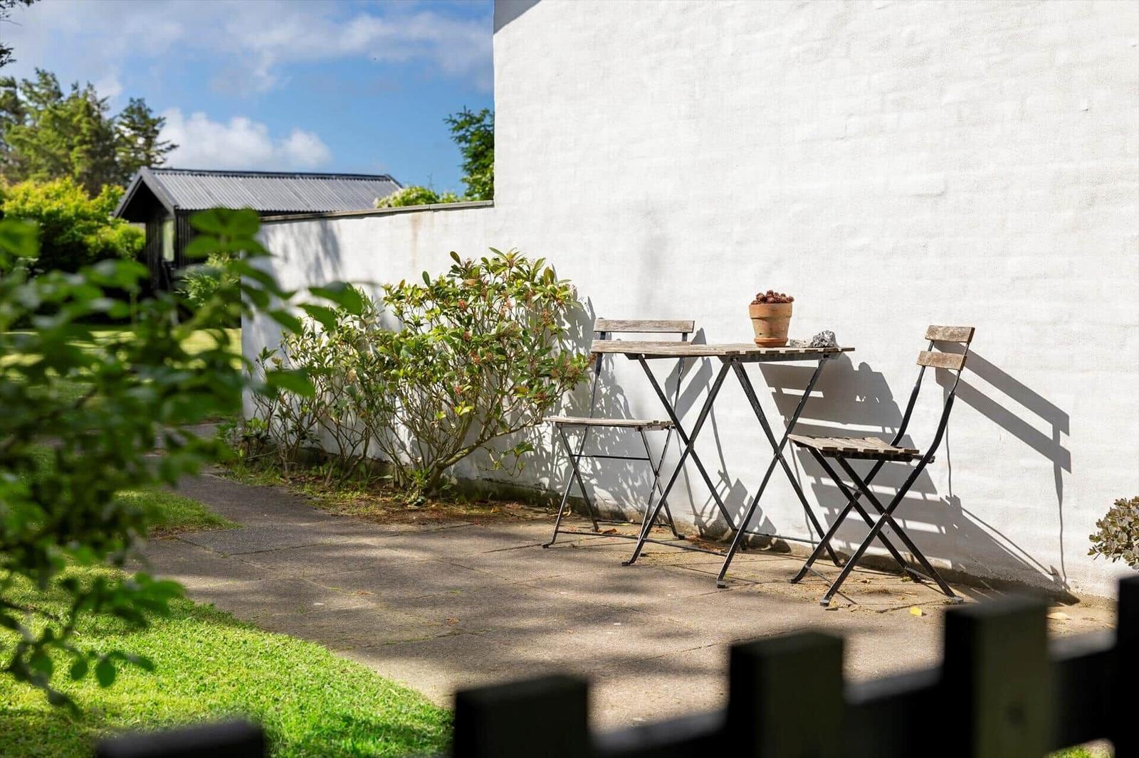 Ein kleiner Gartenbereich mit Tisch und zwei Stühlen an einer weißen Wand.