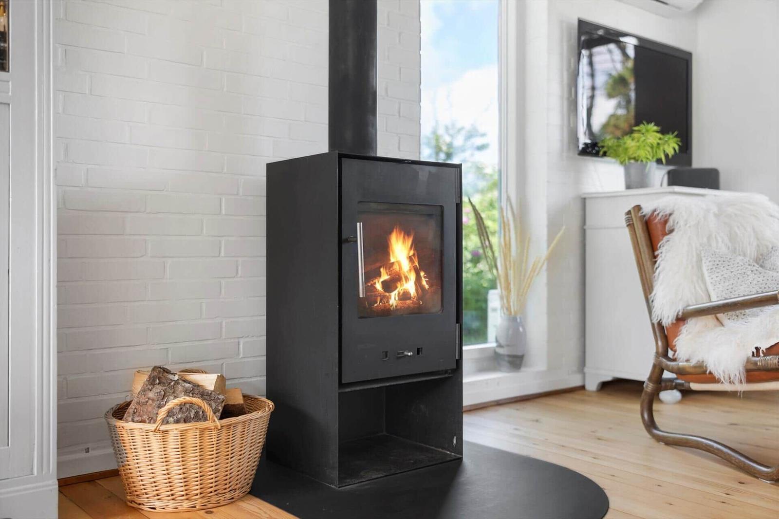 Kaminofen mit brennendem Holz, Korb mit Brennholz, Fernseher und Sessel im Wohnzimmer.