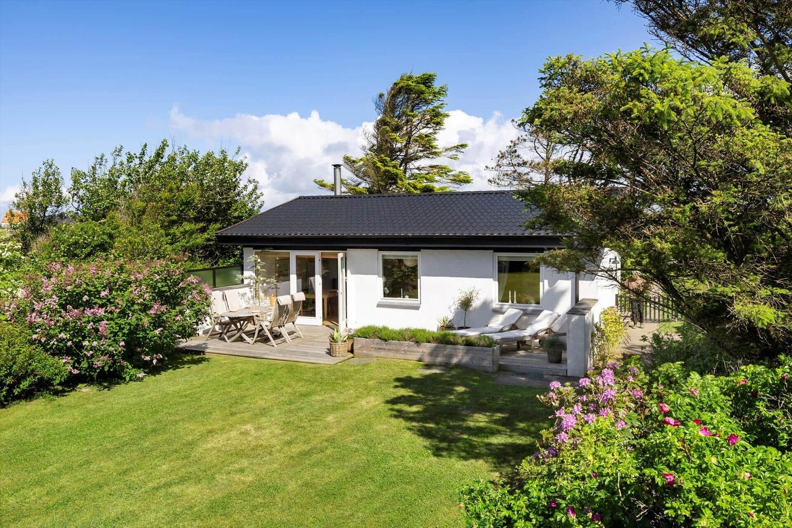 Ein weißes Haus mit Balkon und Garten. Es gibt Liegestühle und einen Tisch mit Stühlen.