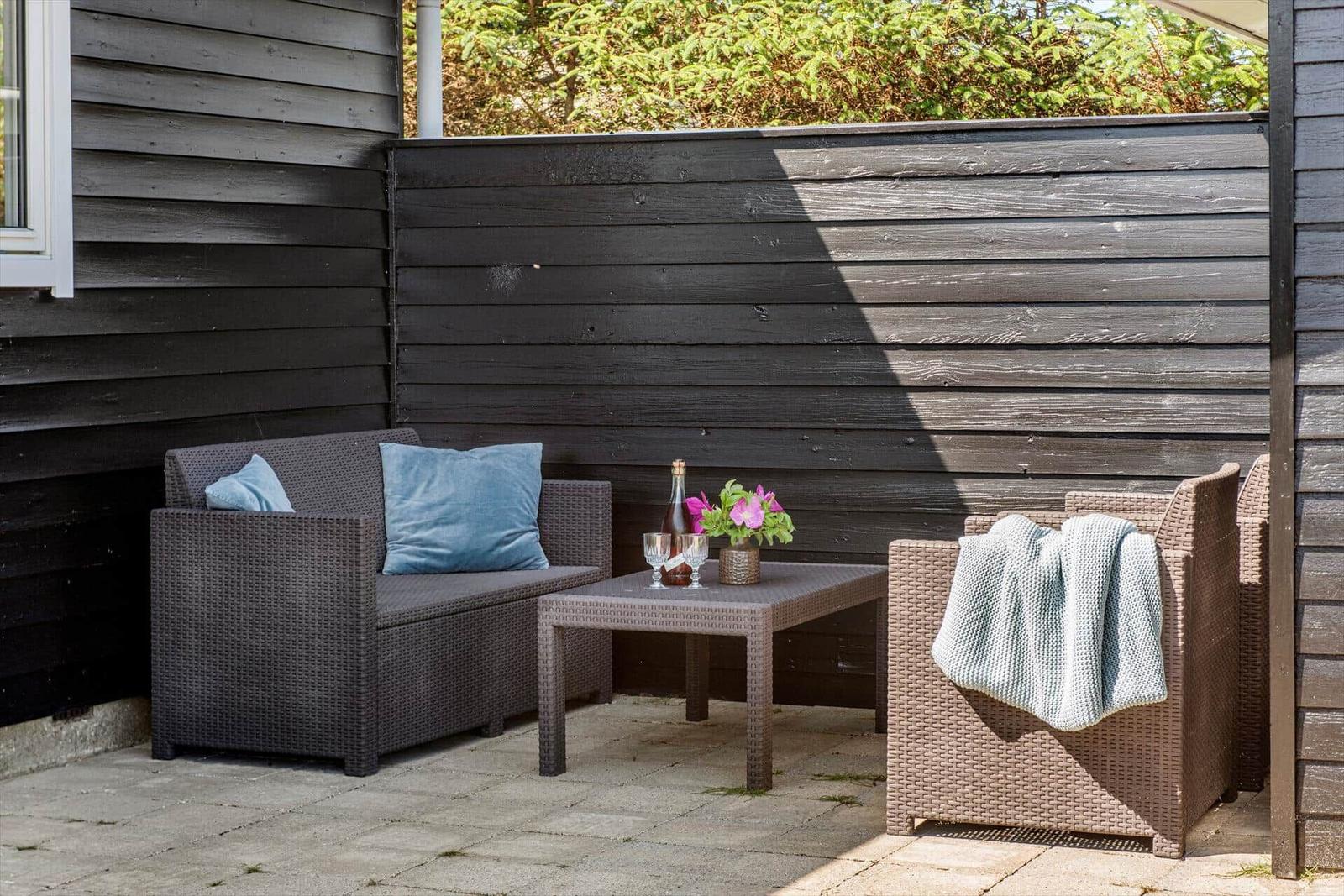 Terrasse mit Gartenmöbeln, Tisch und Blumen vor dunklem Holzhaus