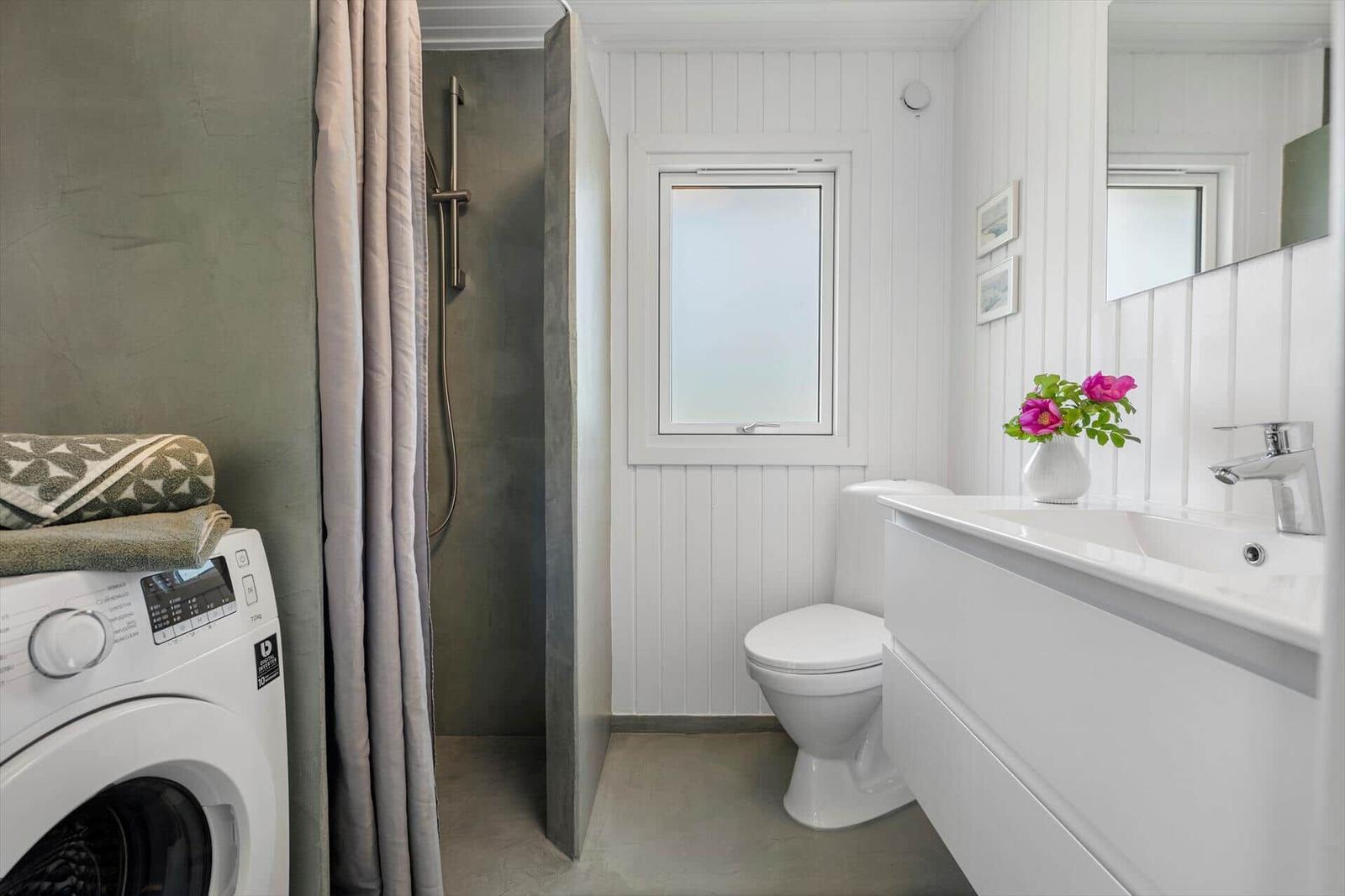 Badezimmer mit Dusche, Toilette und Waschbecken. Weiße Wände, Fenster und Waschtisch.