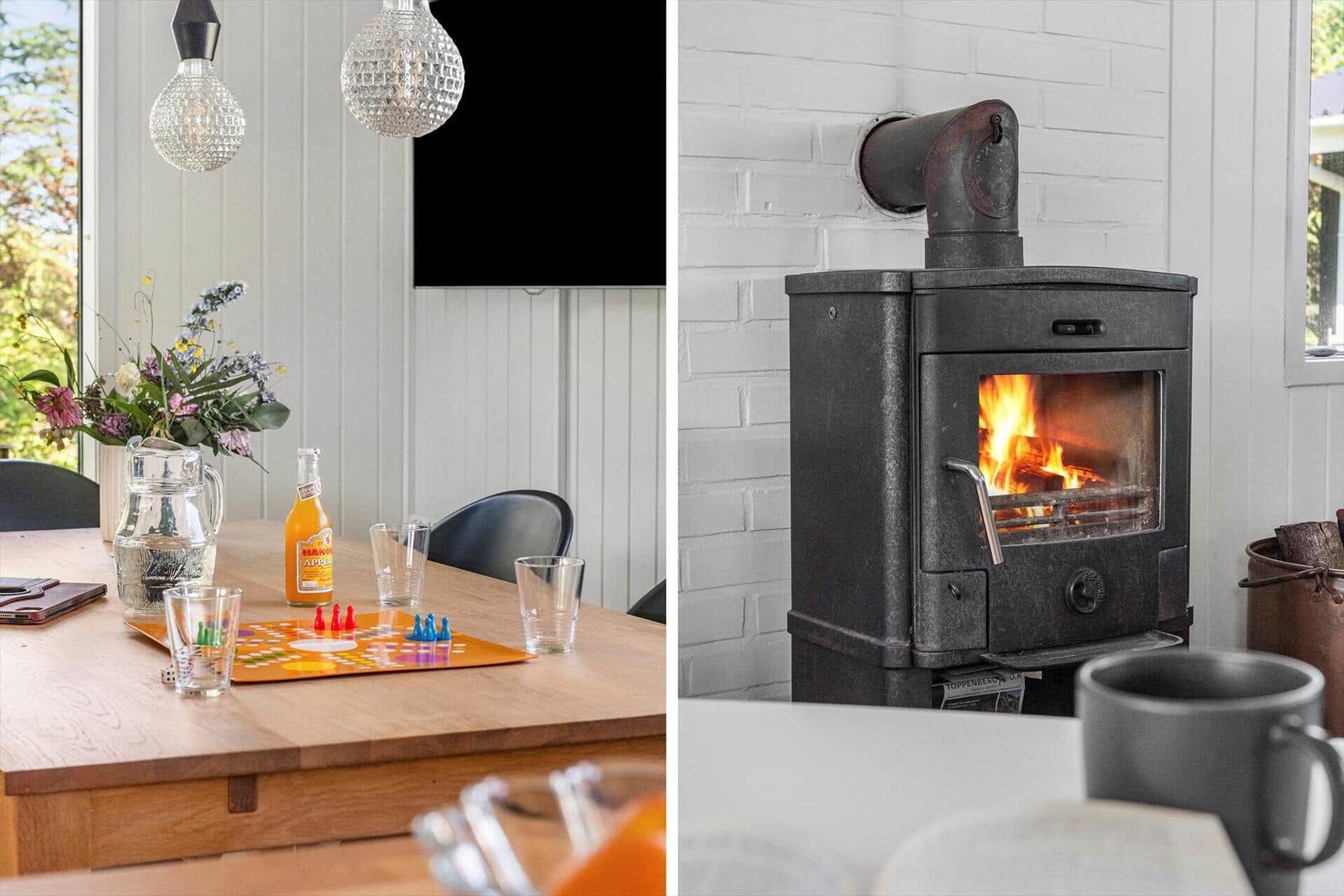 Essbereich mit Tisch, Blumen und Spiel. Kaminofen mit brennendem Holz.