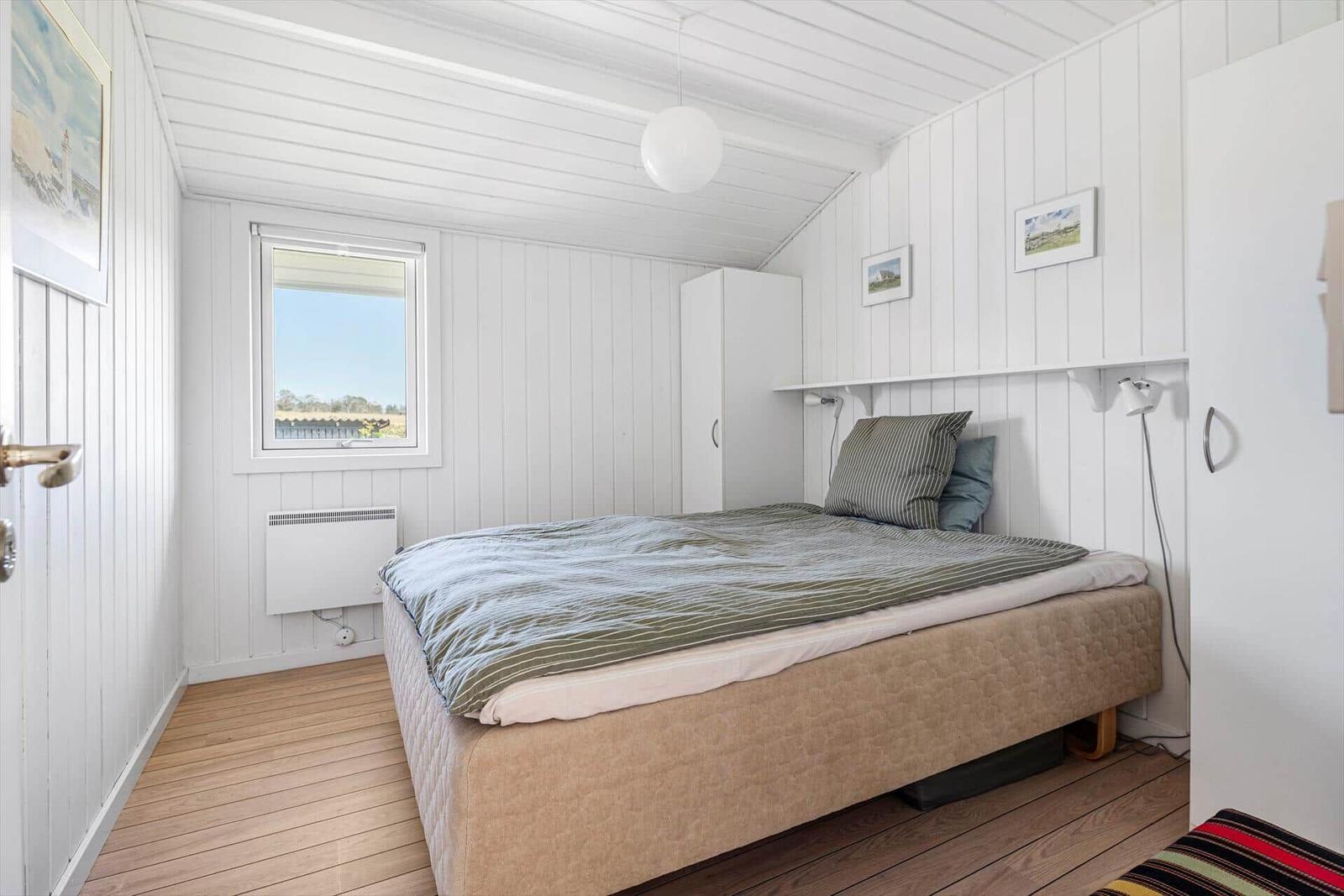 Schlafzimmer mit Bett, Fenster und weißen Wänden.