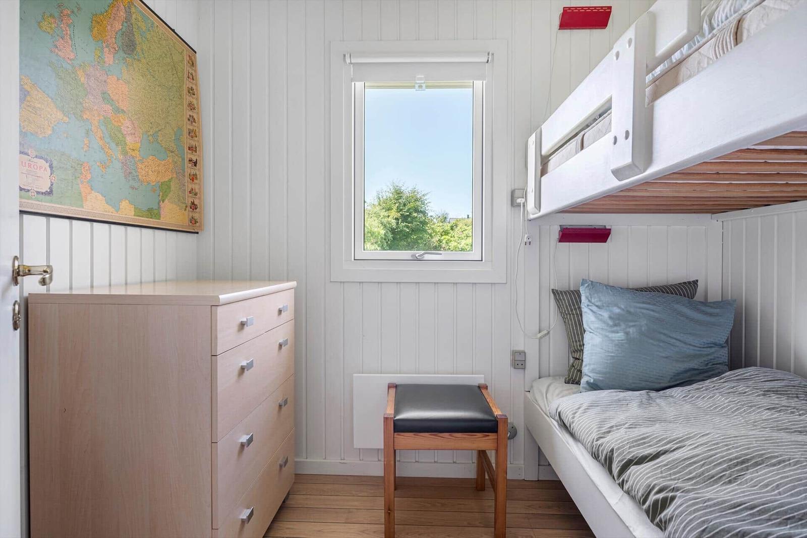 Zimmer mit Doppelstockbett, Schrank und Fenster mit Blick auf Bäume.