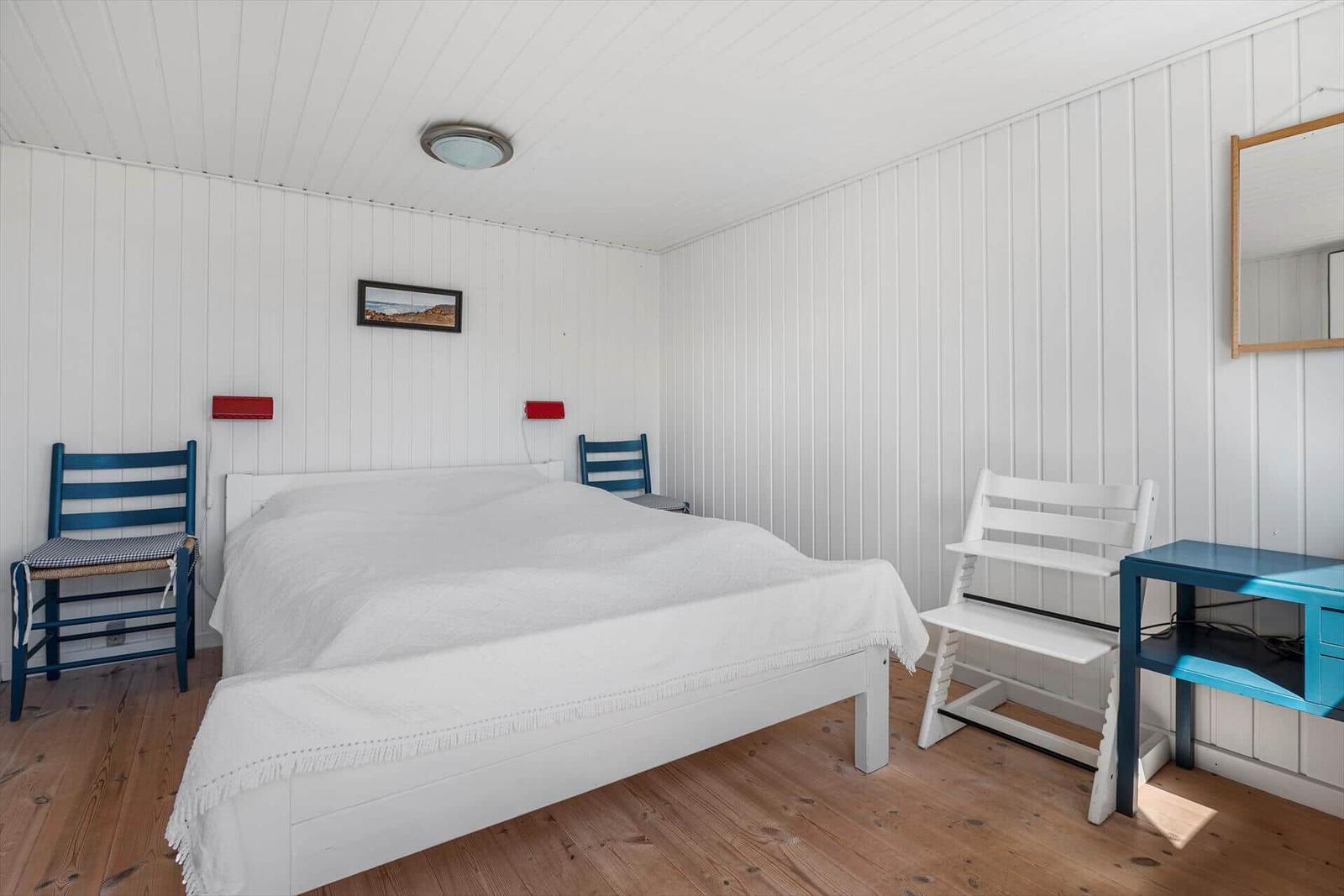 Ein Schlafzimmer mit weißem Bett, blauen Stühlen und Holzboden.