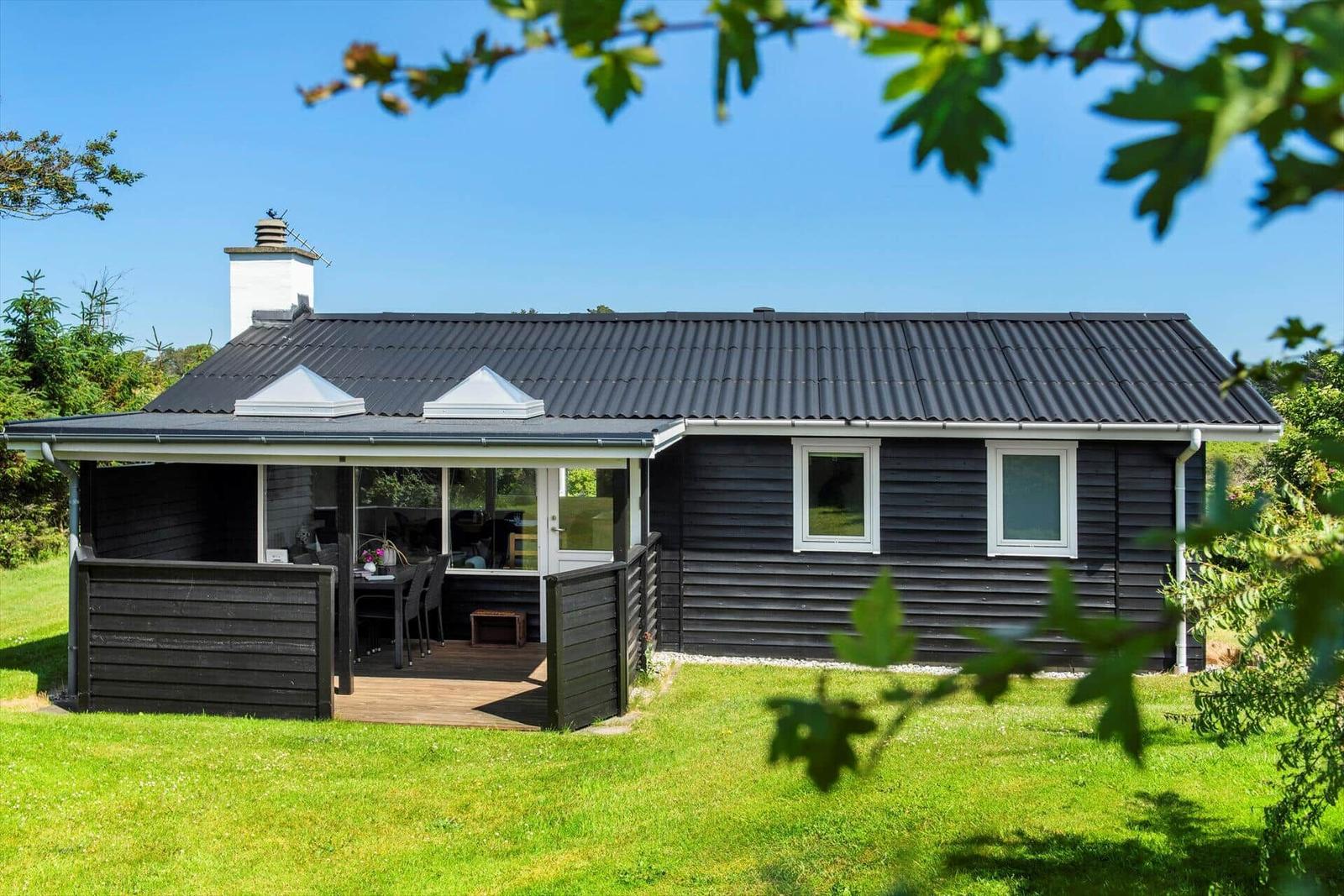 Ein schwarz verputztes Haus mit Terrasse und Gartentisch unter blauem Himmel.