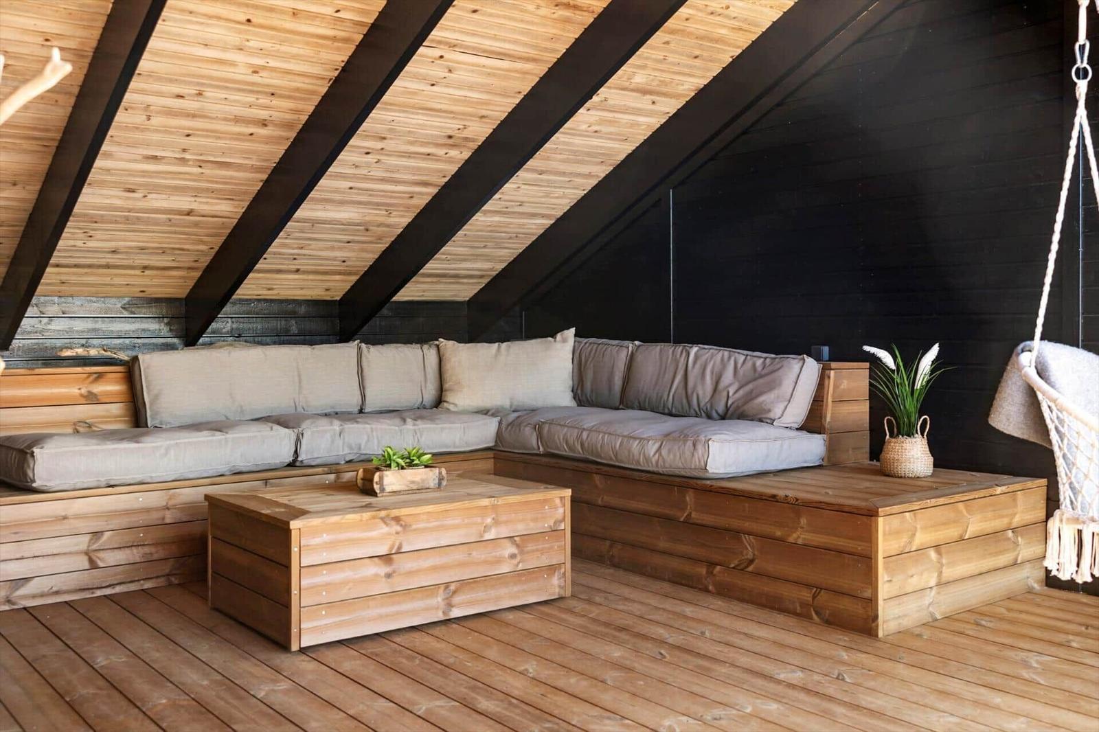 Holzveranda mit Sitzbank, Tisch und Hängesessel. Dachbodenstruktur mit Holz- und schwarzen Elementen.