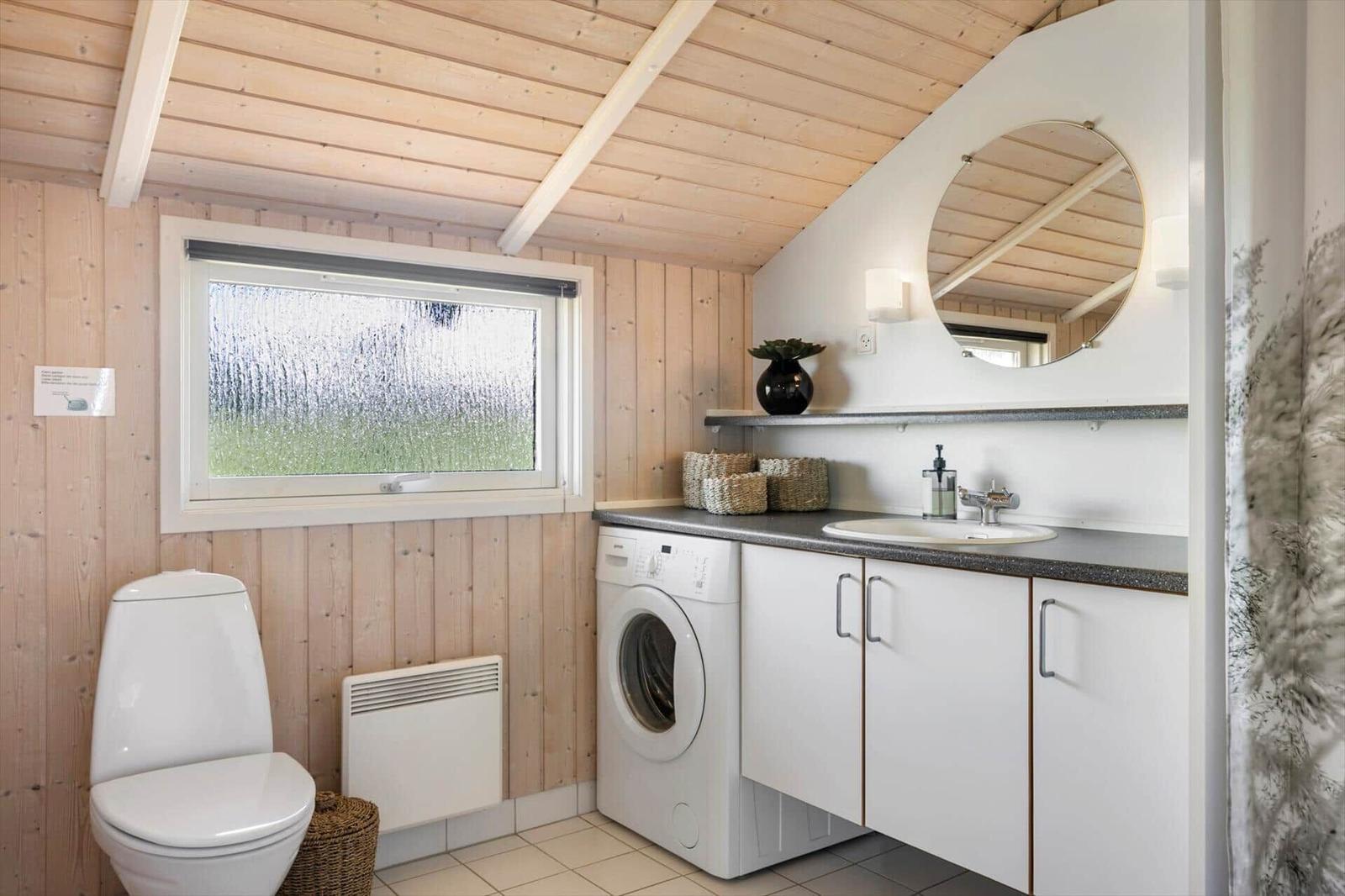 Badezimmer mit Waschmaschine, Waschbecken und Toilette unter Holzdecke.