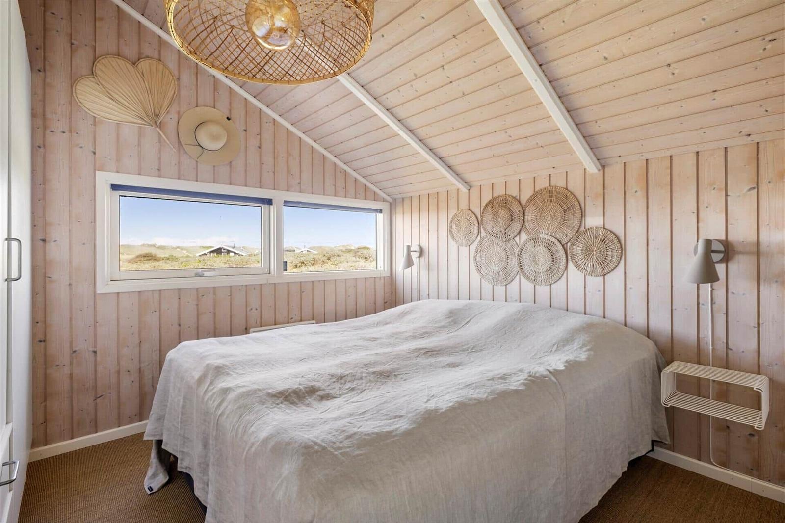 Schlafzimmer mit Holzwand, Bett und Fenster zum Strand