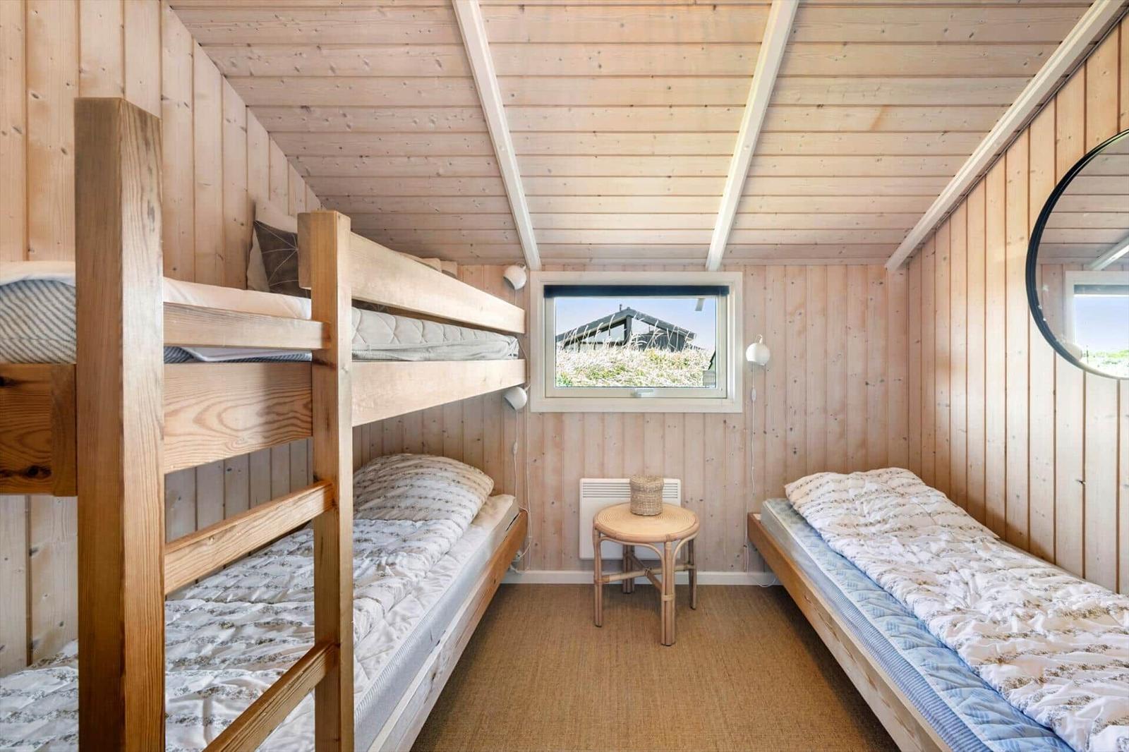 Schlafzimmer mit Holzwänden, Doppelstockbett und Einzelbett. Fenster mit Blick auf Gebäude.