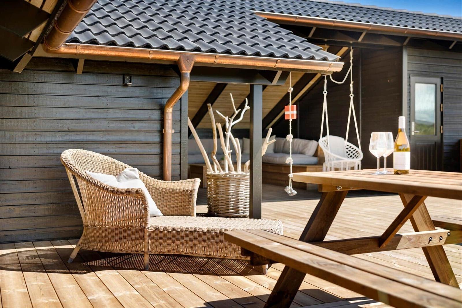 Terrasse mit Holztisch, Wickerliege und Schaukel unter Dach