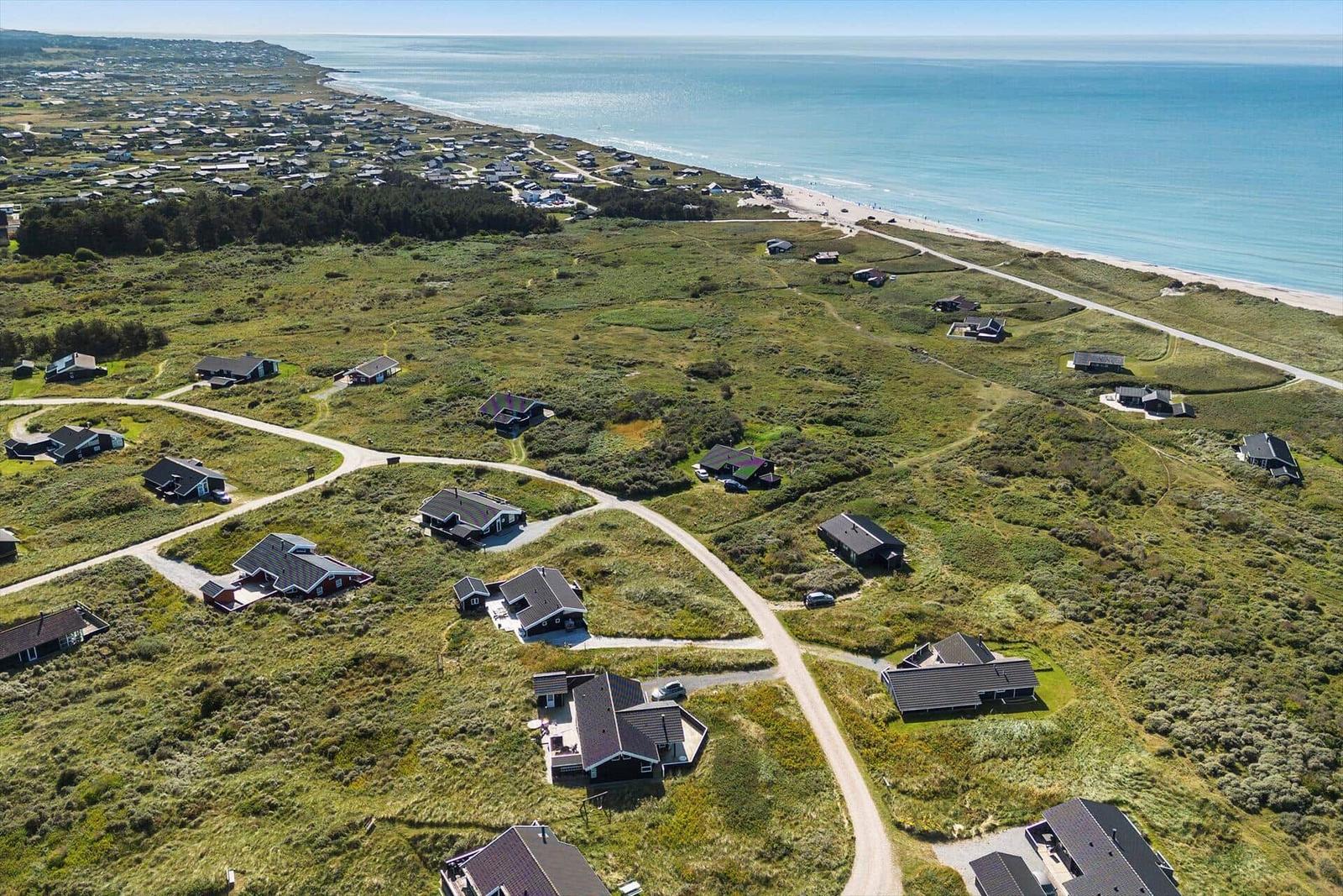 Aerial view of coastal vacation homes with green dunes and beach.