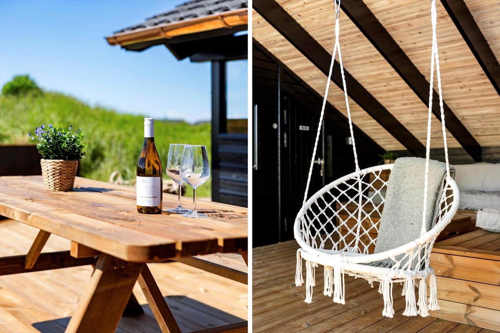 Holztisch mit Weißwein und Gläsern auf Terrasse. Hängesessel mit Decke unter Dach.