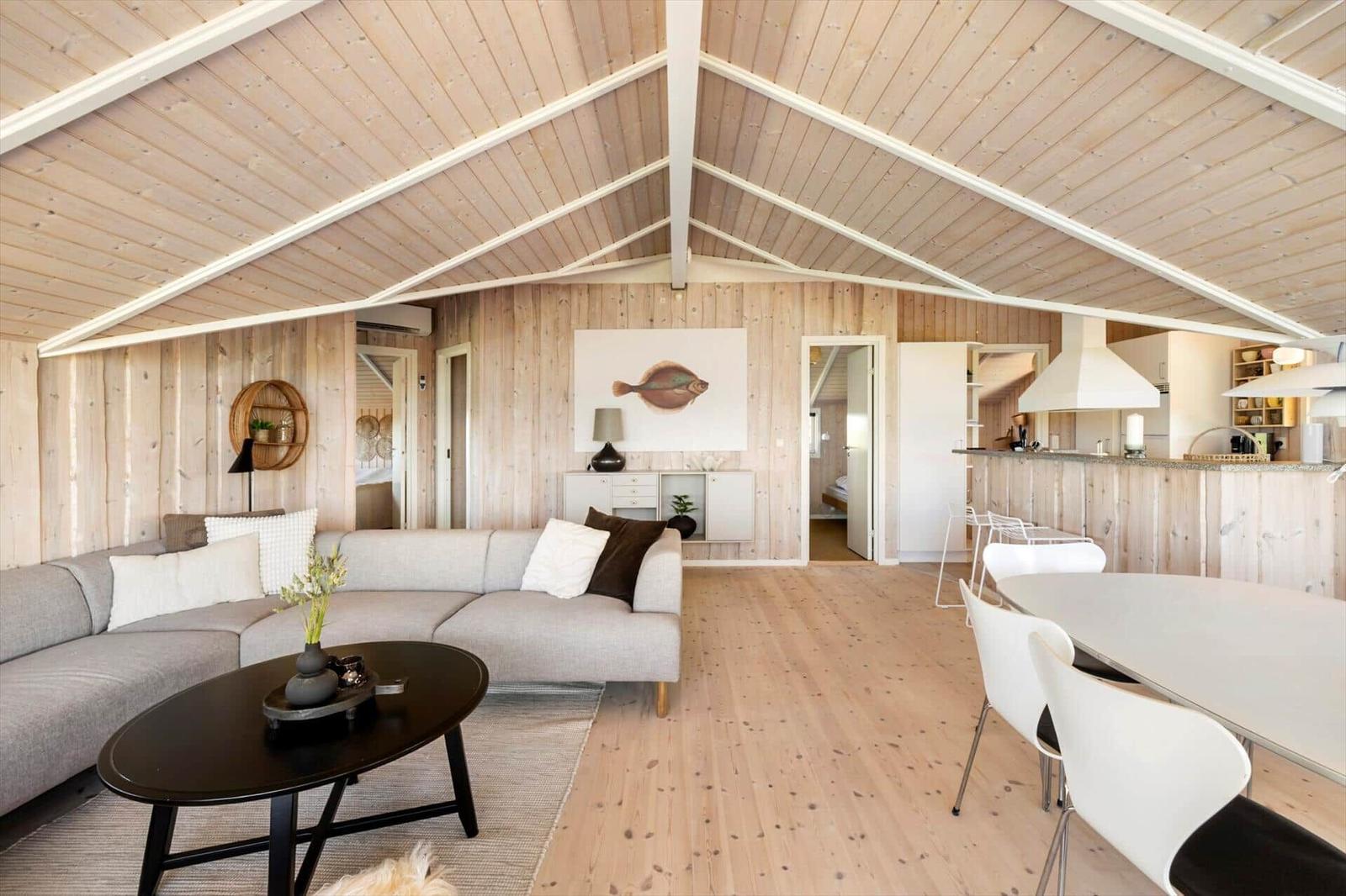 Wohnzimmer mit Sofa, Esstisch und Küche unter Holzdecke.