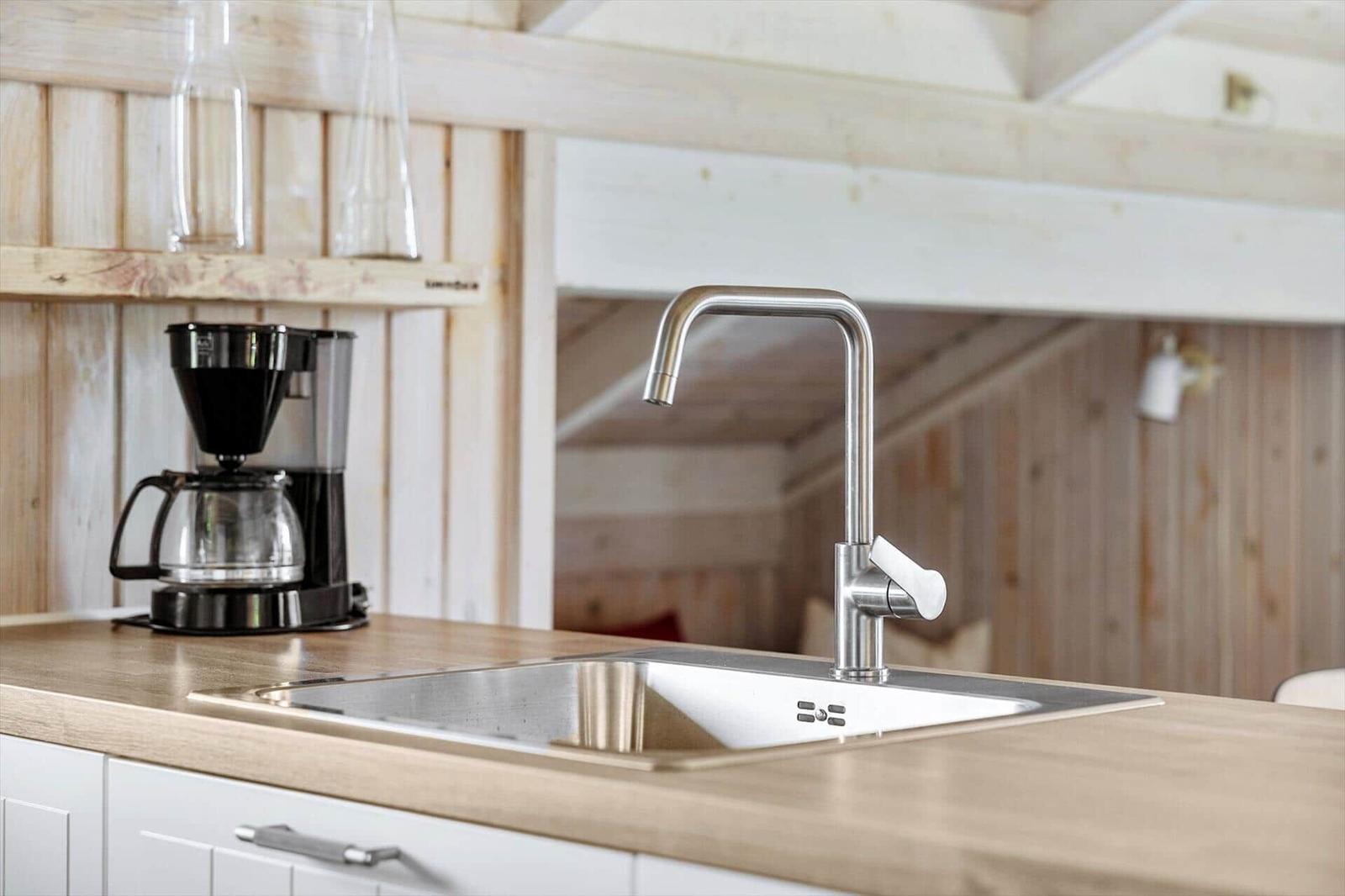 Küchenbereich mit Edelstahl-Spüle und Wasserhahn, Holzoberfläche und Kaffeemaschine.