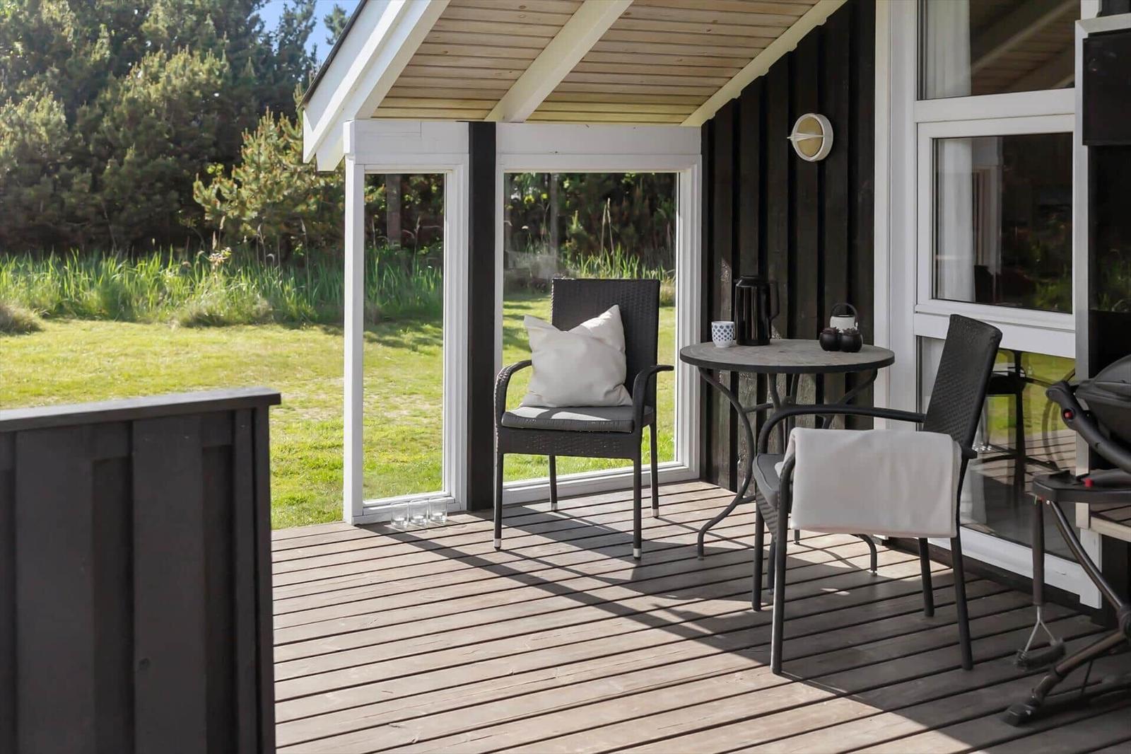 Terrasse mit Tisch, zwei Stühlen und Grill. Blick auf grünen Garten.