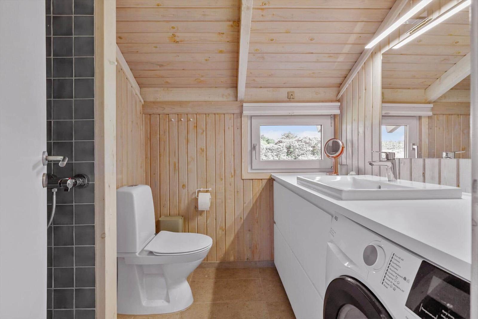 Badezimmer mit Toilette, Waschmaschine und Fenster mit Blick nach draußen.