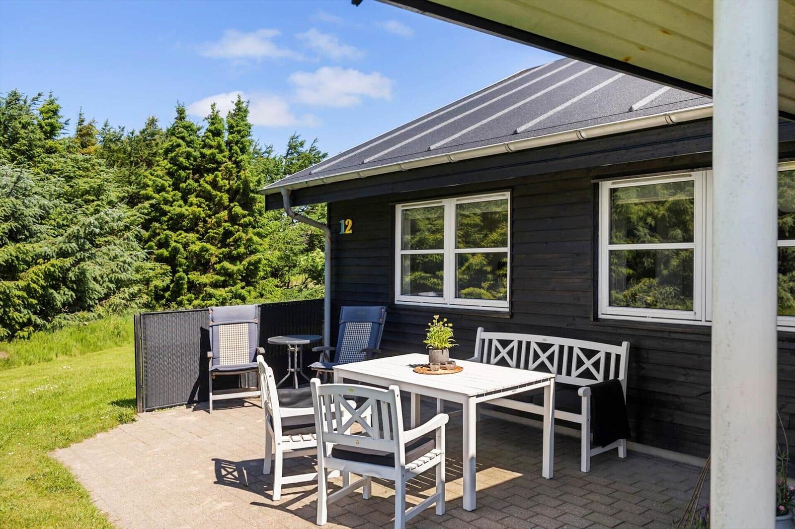 Terrasse mit weißem Tisch und Stühlen vor einem dunkelbraunen Haus mit Fenstern.