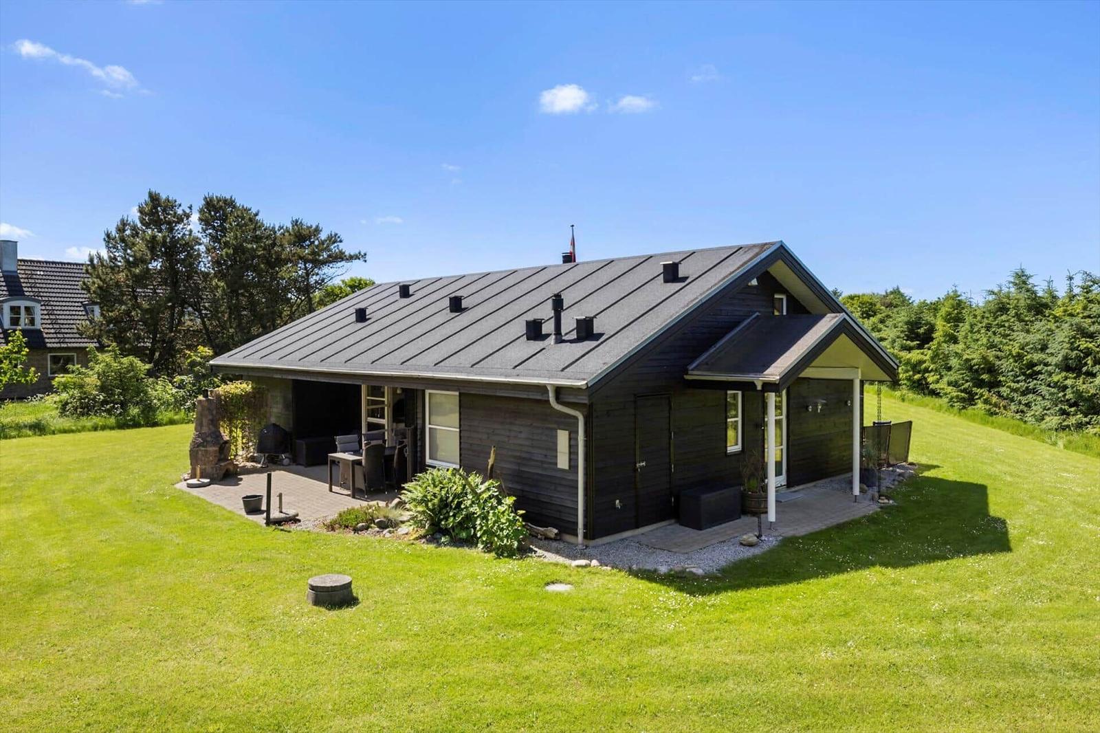 Ein modernes Holzhaus mit Terrasse und Garten. Hintergrund: Bäume und blauer Himmel.