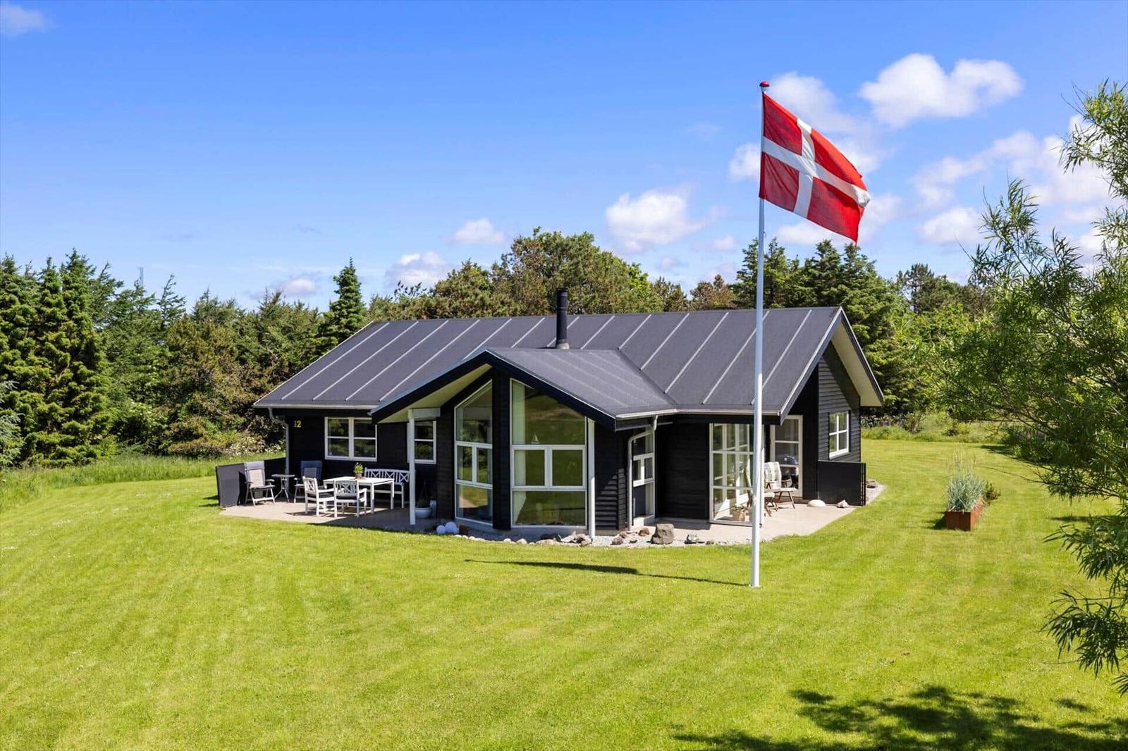 Schwarzes Haus mit großem Garten und dänischer Flagge. Terrasse mit Tisch und Stühlen.