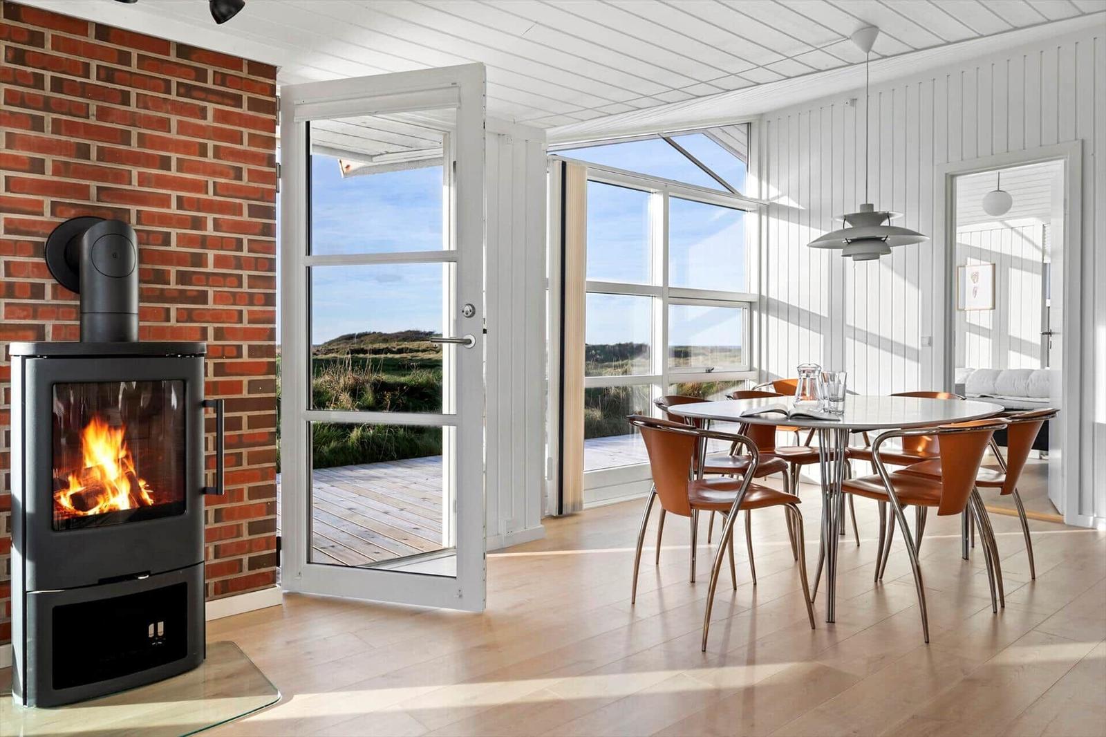 Raum mit Esstisch, Holzfußboden und Kaminofen an Backsteinwand. Durchgang zur Terrasse mit Blick auf Landschaft.