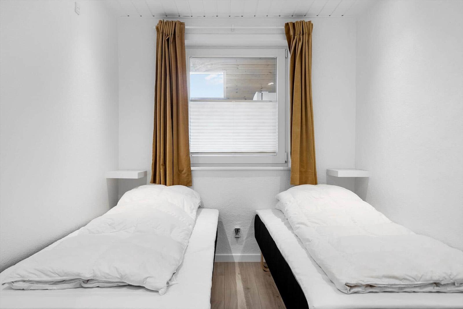 Zwei Betten mit weißen Bettwäsche unter einem Fenster mit braunen Vorhängen.