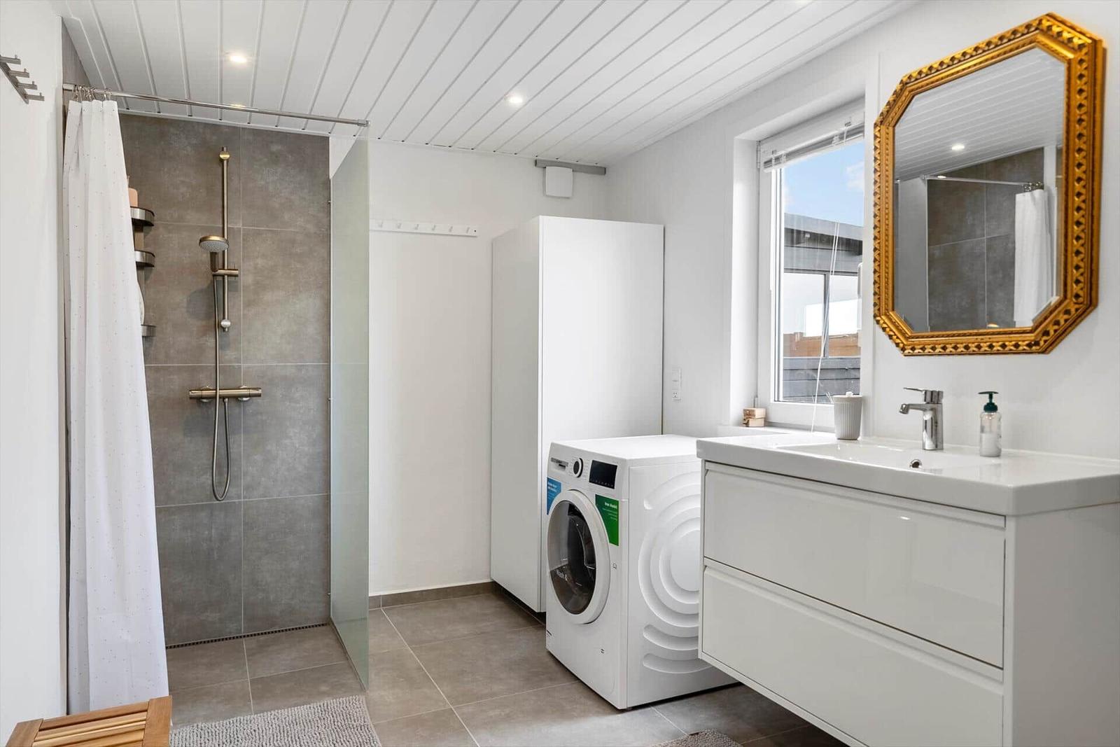 Badezimmer mit Dusche, Waschmaschine und Spiegelschrank.