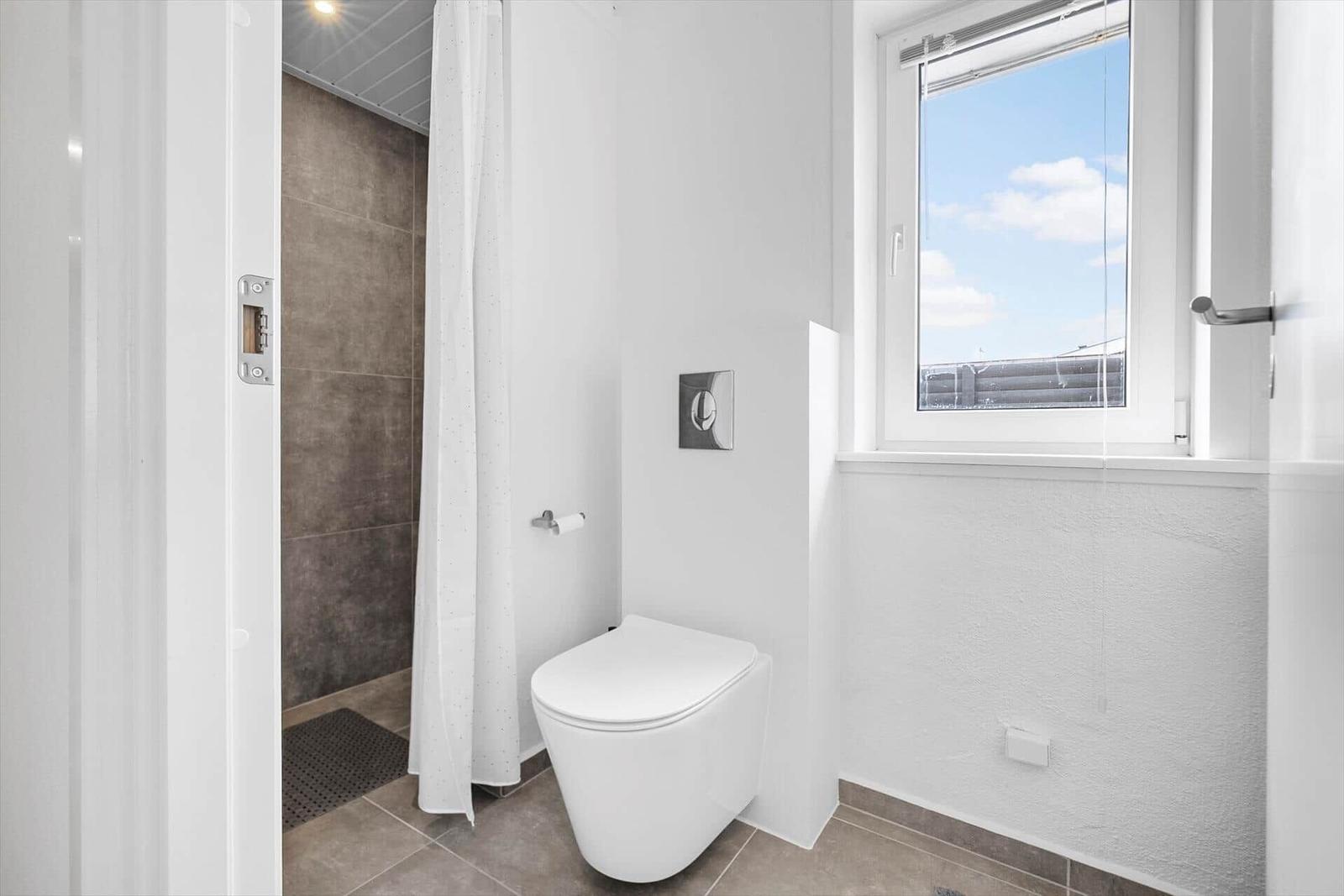 Badezimmer mit Toilette, Dusche und Fenster mit Blick nach draußen.