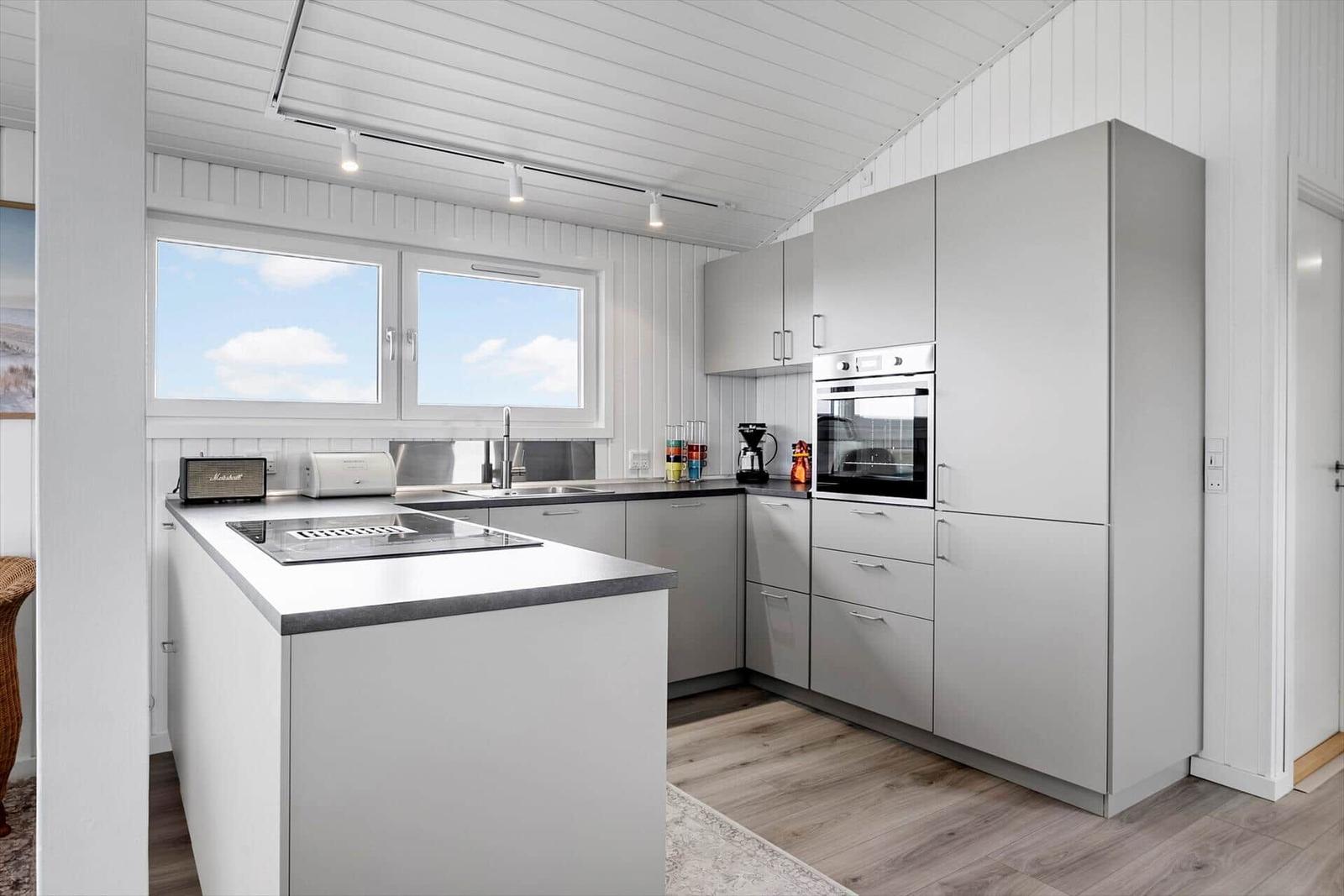 Moderne Küche mit Arbeitsinsel, Dunstabzug, Backofen und Fenstern.