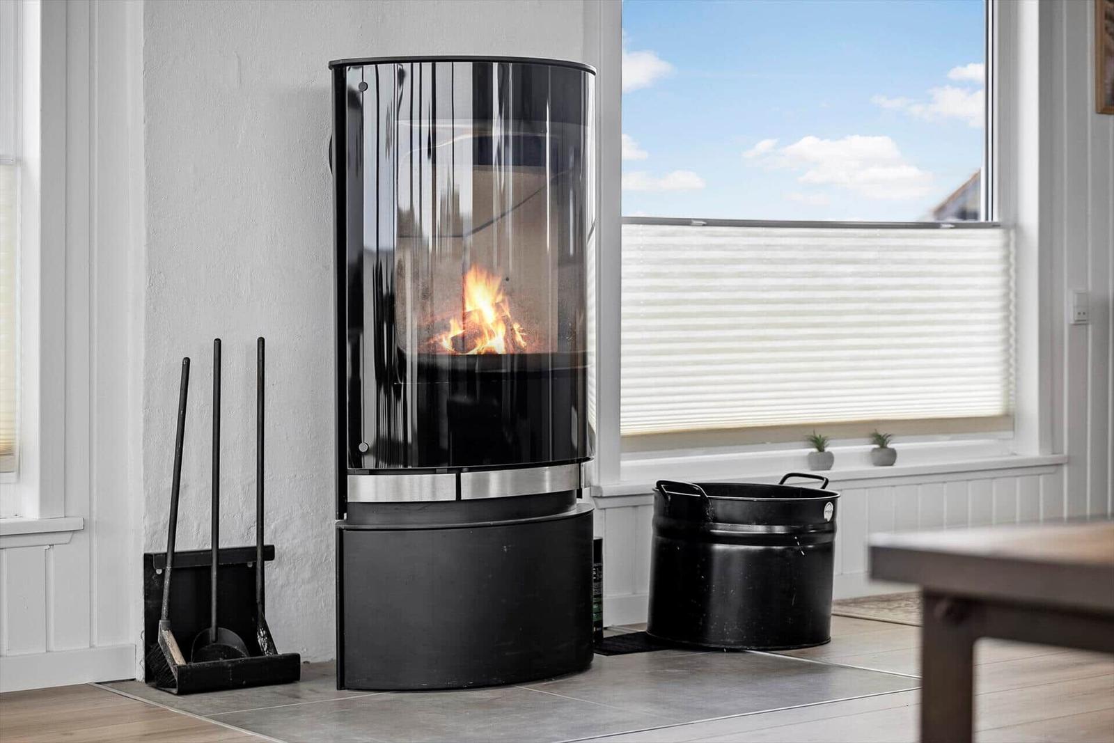Moderne Feuerstelle mit brennendem Holz, daneben steht ein schwarzer Eimer.