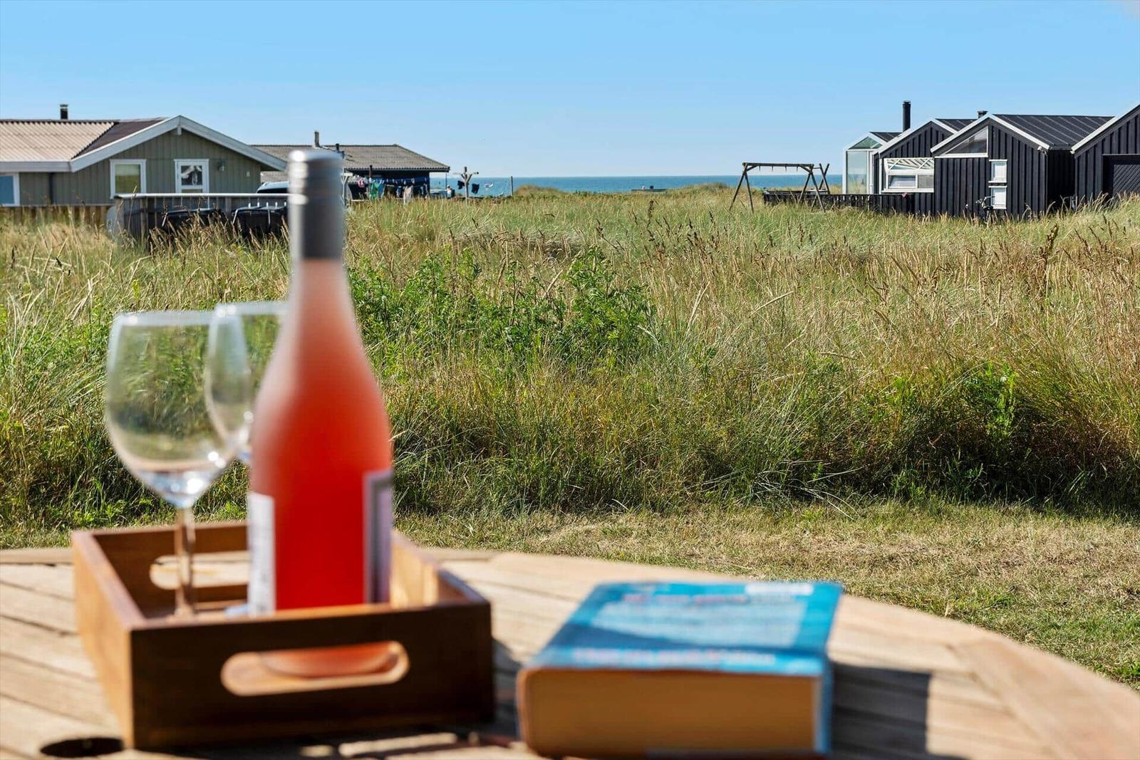 Roséwein und Buch auf Tisch mit Blick auf Strandhäuser und Grasland.