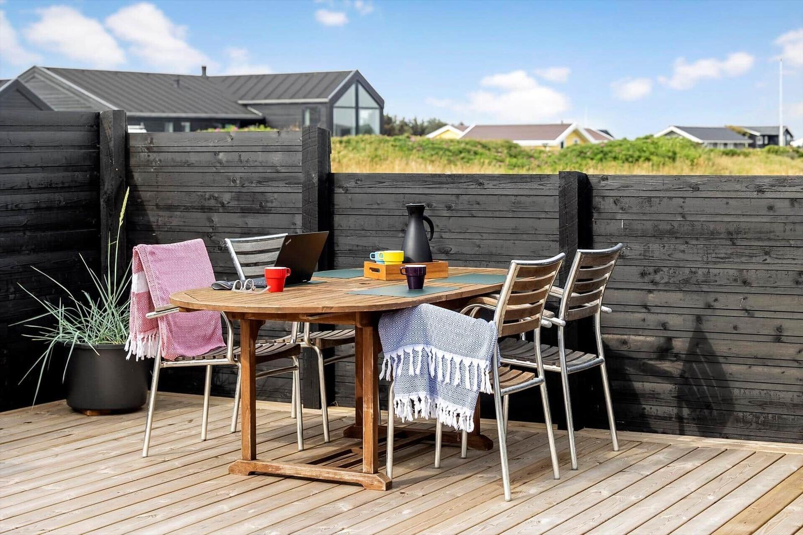 Terrasse mit Holztisch, Stühlen und Decken. Hintergrund: Holzzaun und Häuser.