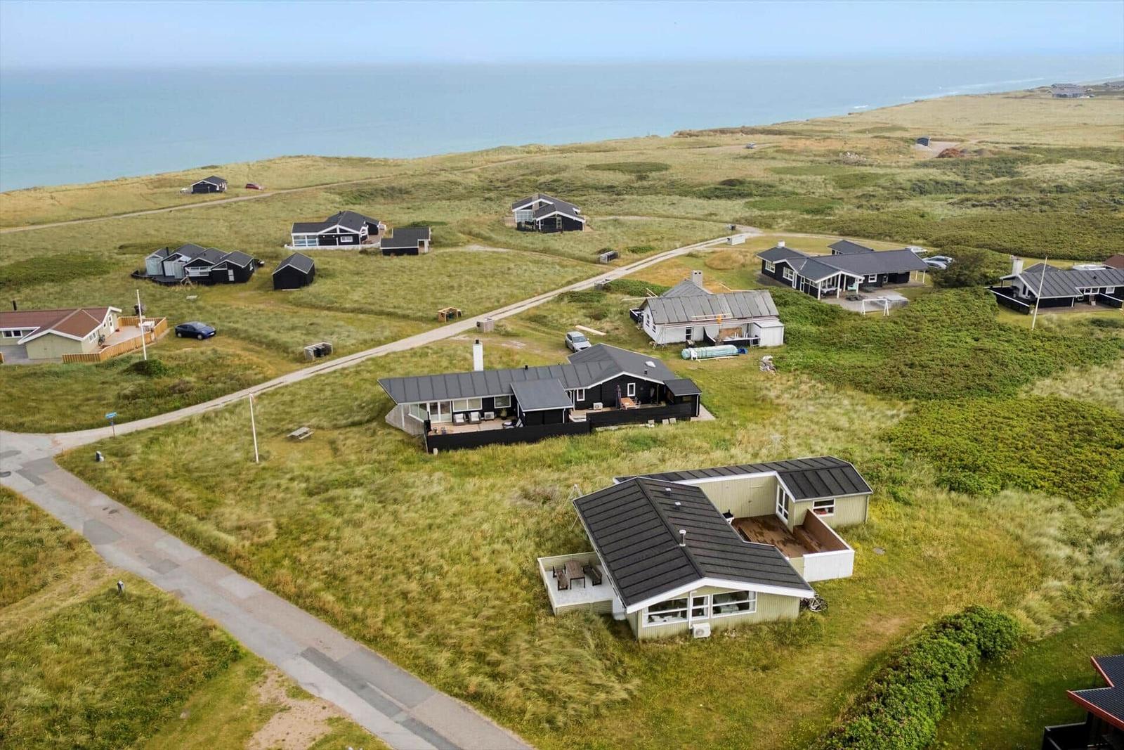 Meerblick auf mehrere Häuser in einer grünen Landschaft mit Wegen und einem Strand.