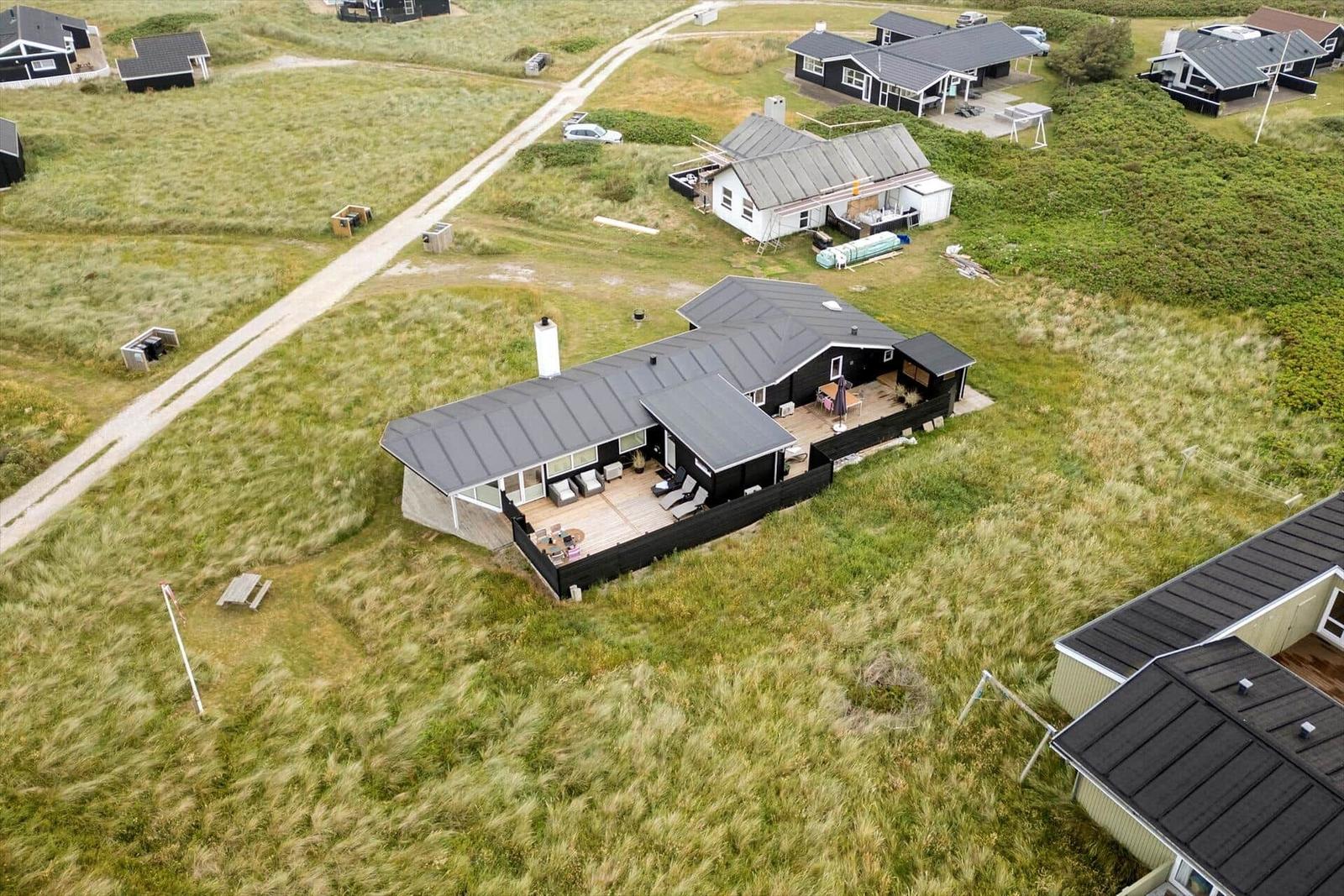 Modernes Ferienhaus mit Terrasse und Garten. Umgeben von Grasflächen und weiteren Häusern.