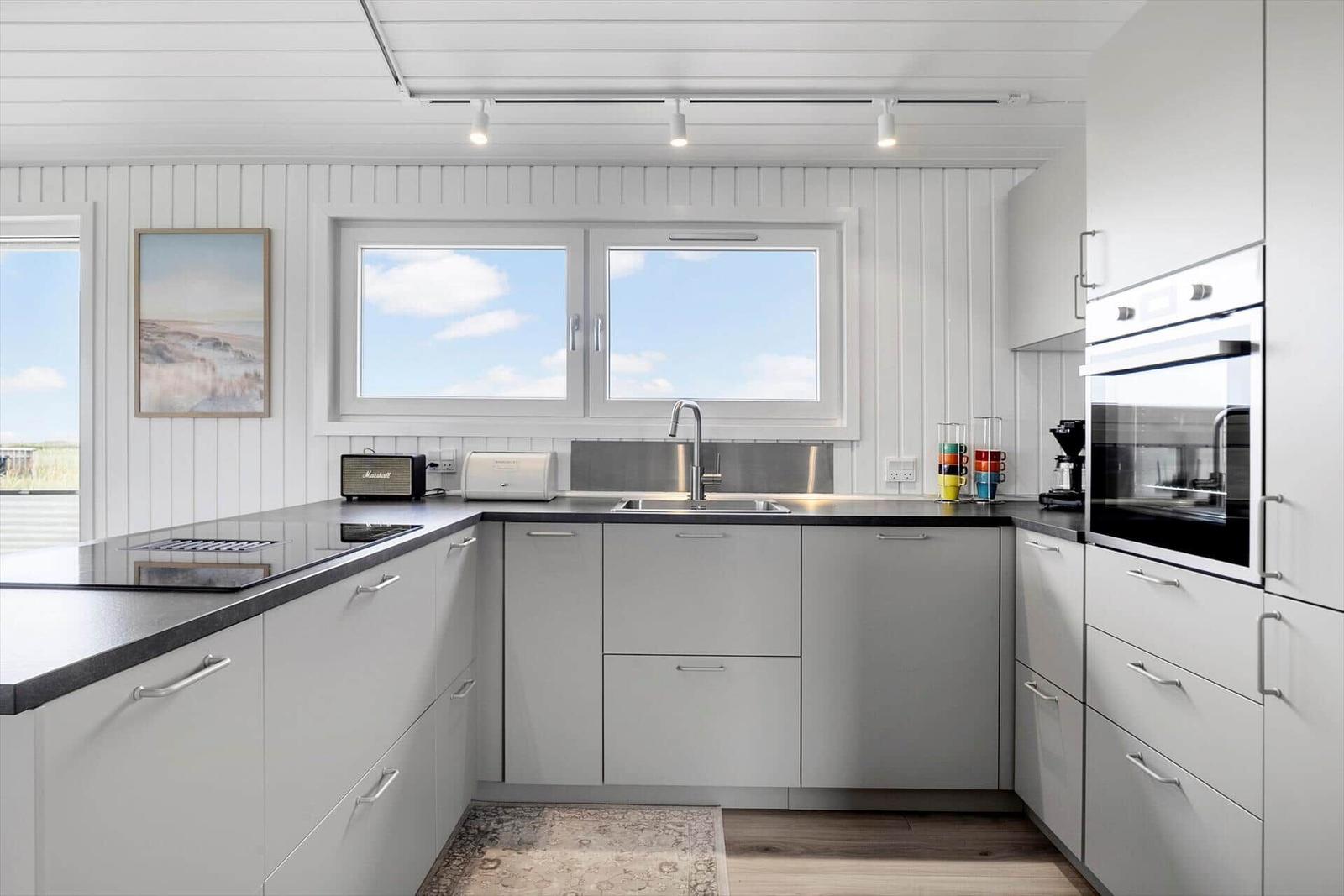 Moderne Küche mit weißen Schränken, dunklem Arbeitsplatz und Fenster mit Blick auf den Himmel.