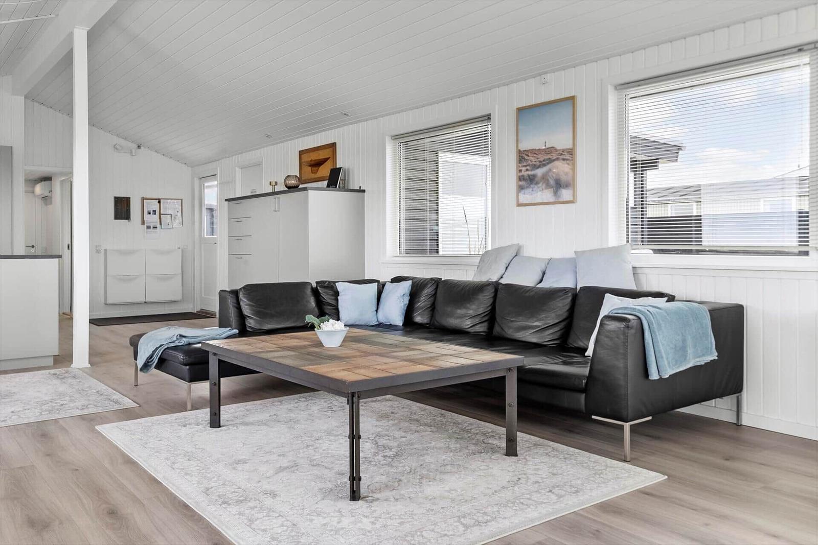 Wohnzimmer mit schwarzer Ledercouch, Holztisch und weißen Wänden.