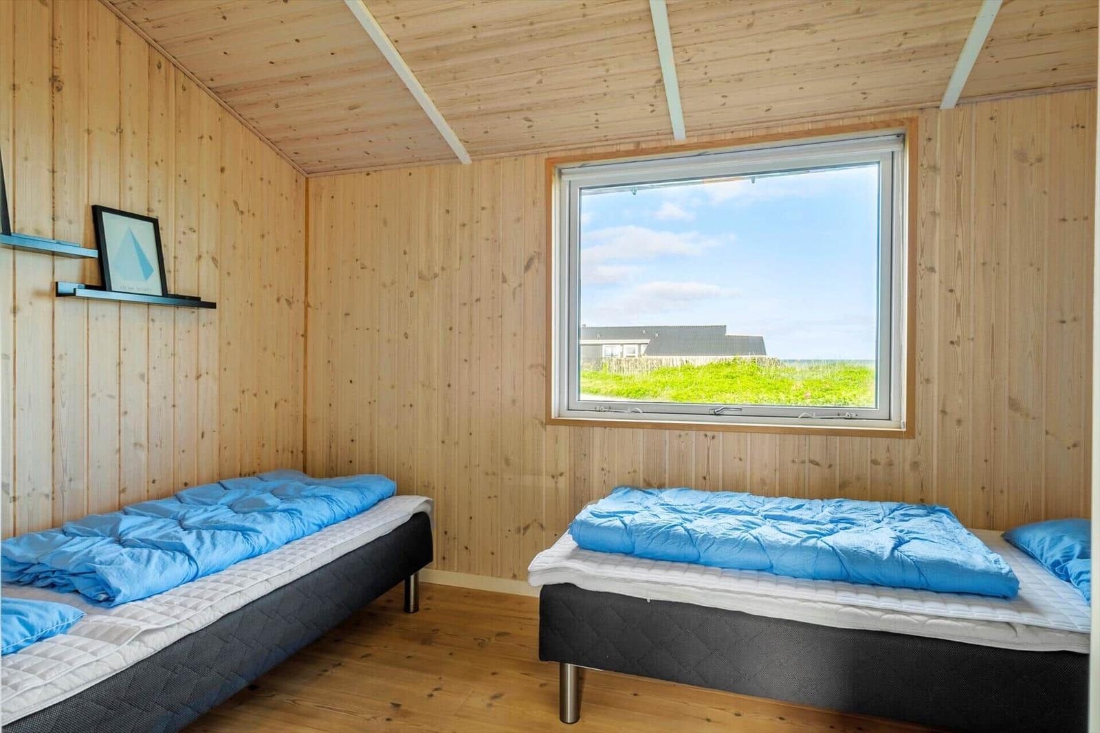 Zwei Betten mit blauen Decken. Holzwände und ein Fenster mit Blick auf Gras und Himmel.
