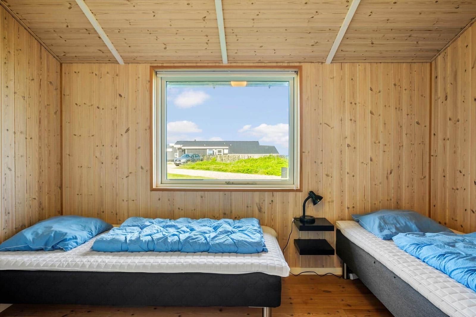 Zwei Betten mit blauen Decken, Holzwände und Fensterblick auf Grünland.