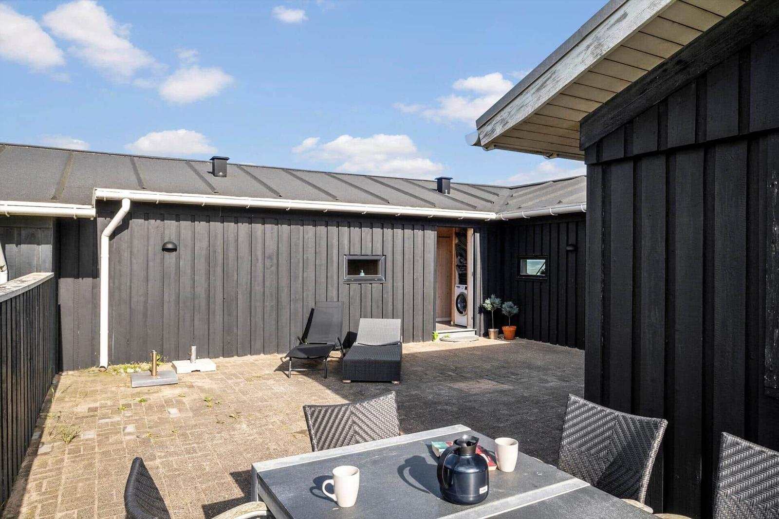 Hinterhof mit Sitzgelegenheiten und Waschmaschine. Schwarze Holzwände und Terrassenbereich.