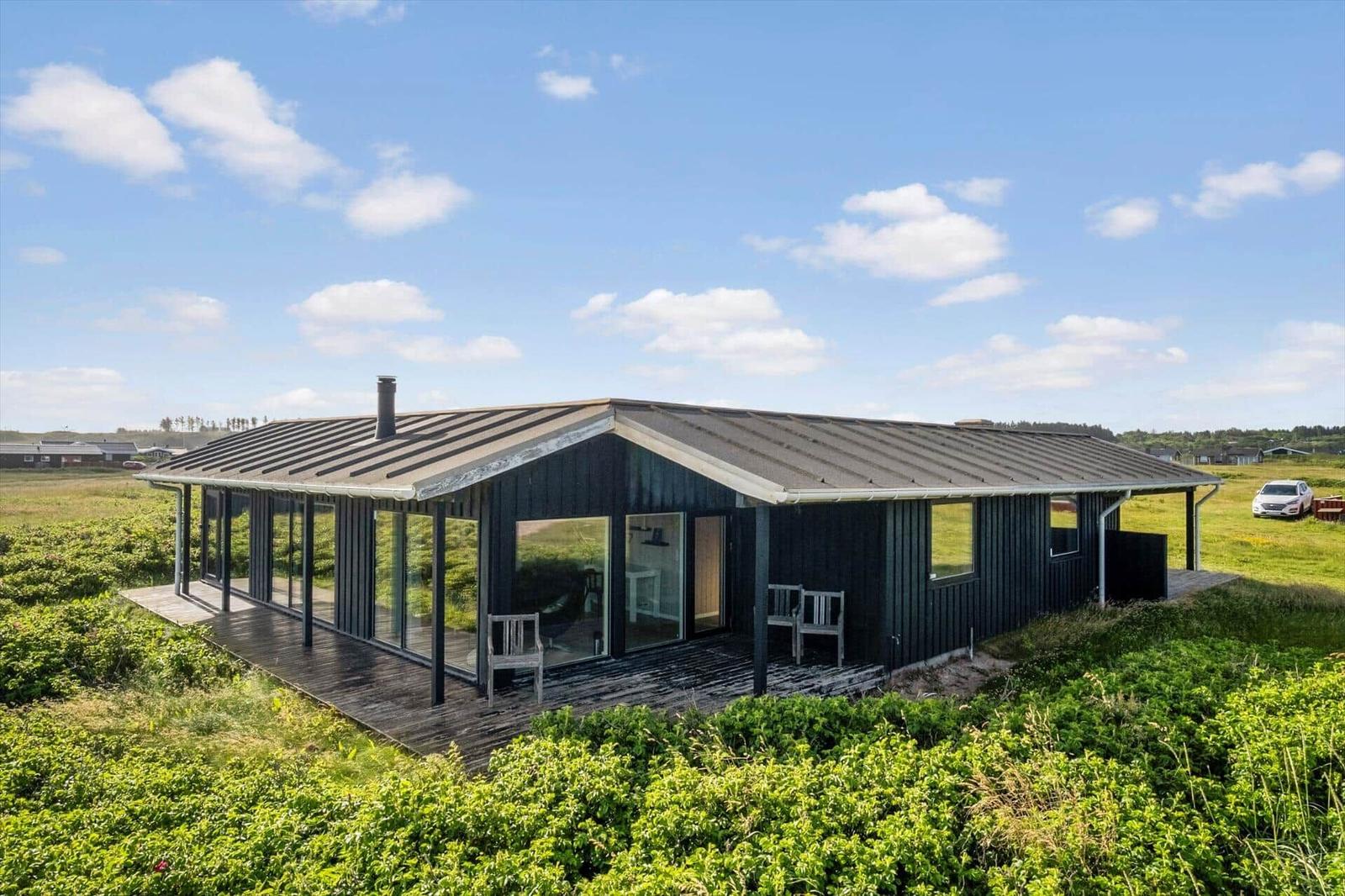 Moderne Villa mit Holzterrasse und großem Glasbereich in grüner Landschaft.